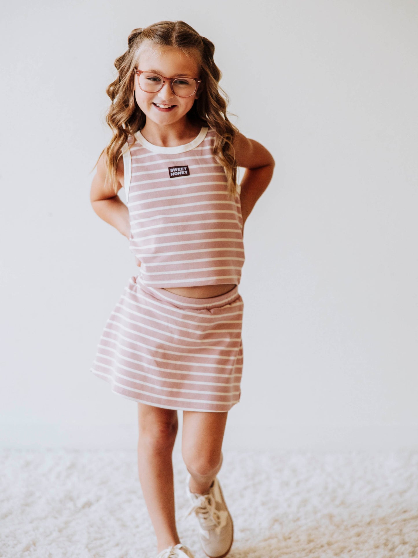 Model is wearing a pink and ivory striped two piece skort set. There is a sweethoney stitched tag on the middle of chest of shirt. 