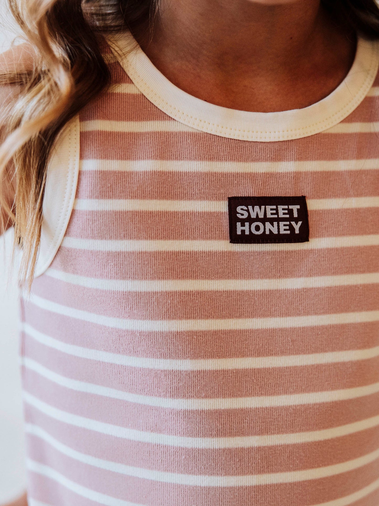 Up close picture of pink and ivory striped shirt that has a black and white sweethoney tag stitched to the middle of shirt. 
