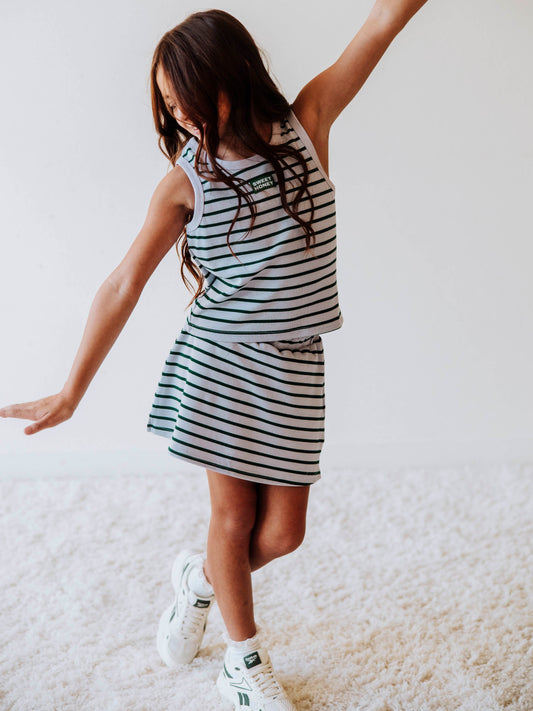 Model is wearing a green and gray striped skort set with a green and white stitched SweetHoney logo tag on center of chest. Model is posing. 