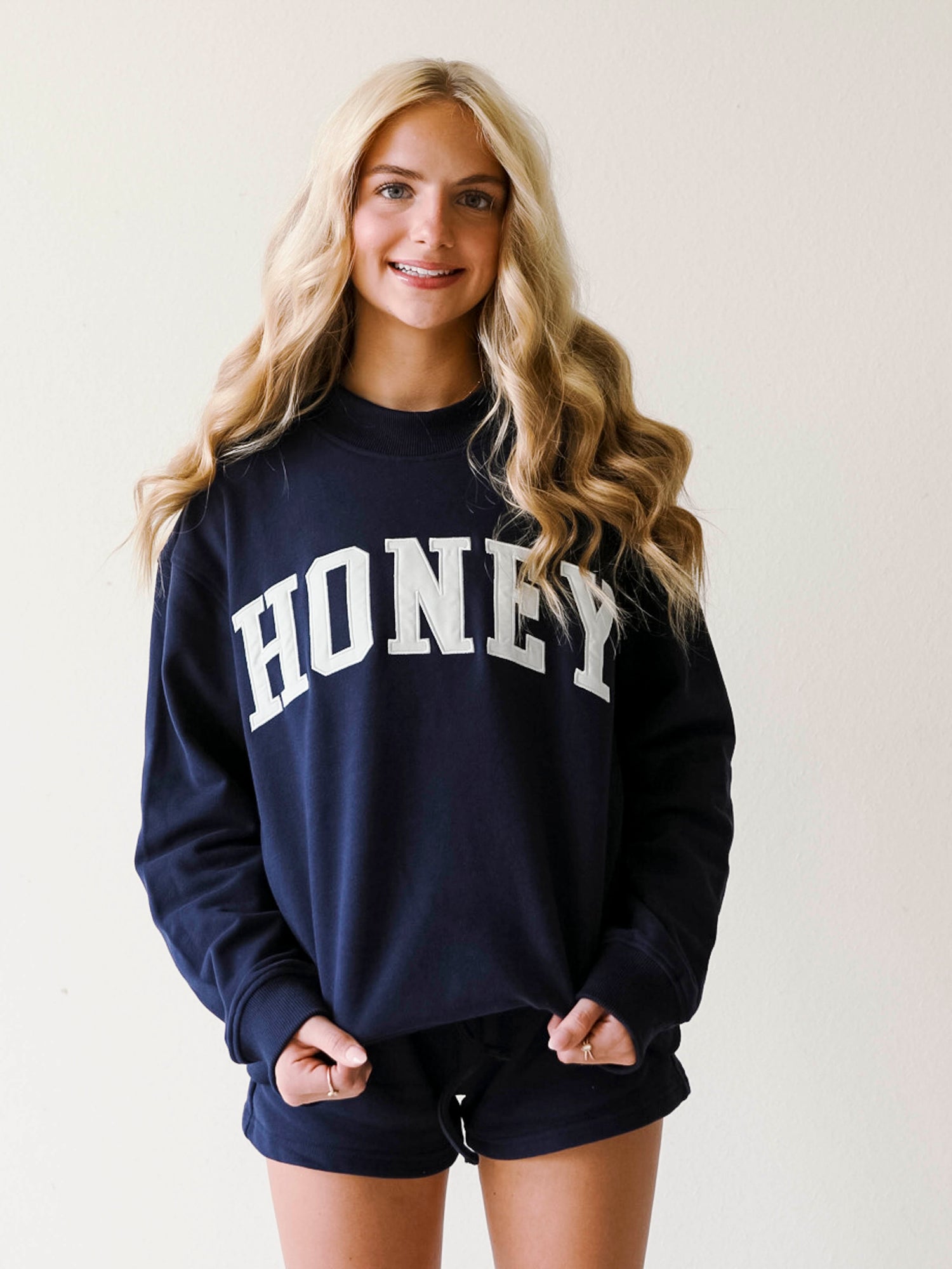 Girl wearing a two piece, navy colored set. The top is a mock neck style that says HONEY on the front and the bottoms are also navy in color.