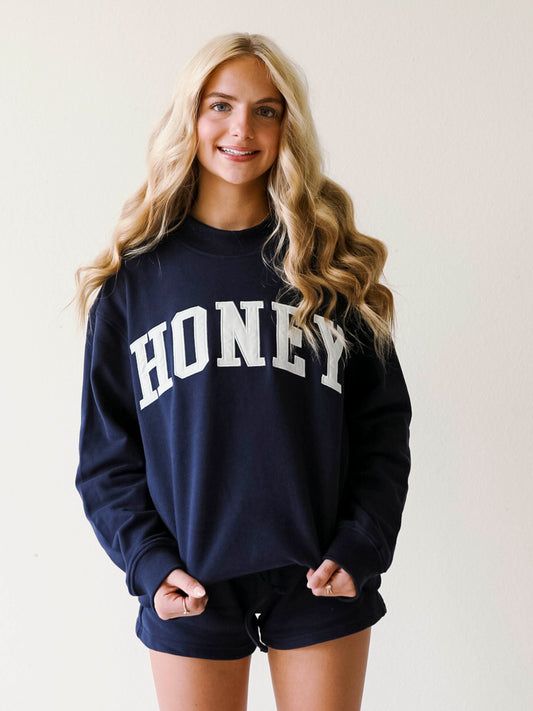 Girl wearing a two piece, navy colored set. The top is a mock neck style that says HONEY on the front and the bottoms are also navy in color.