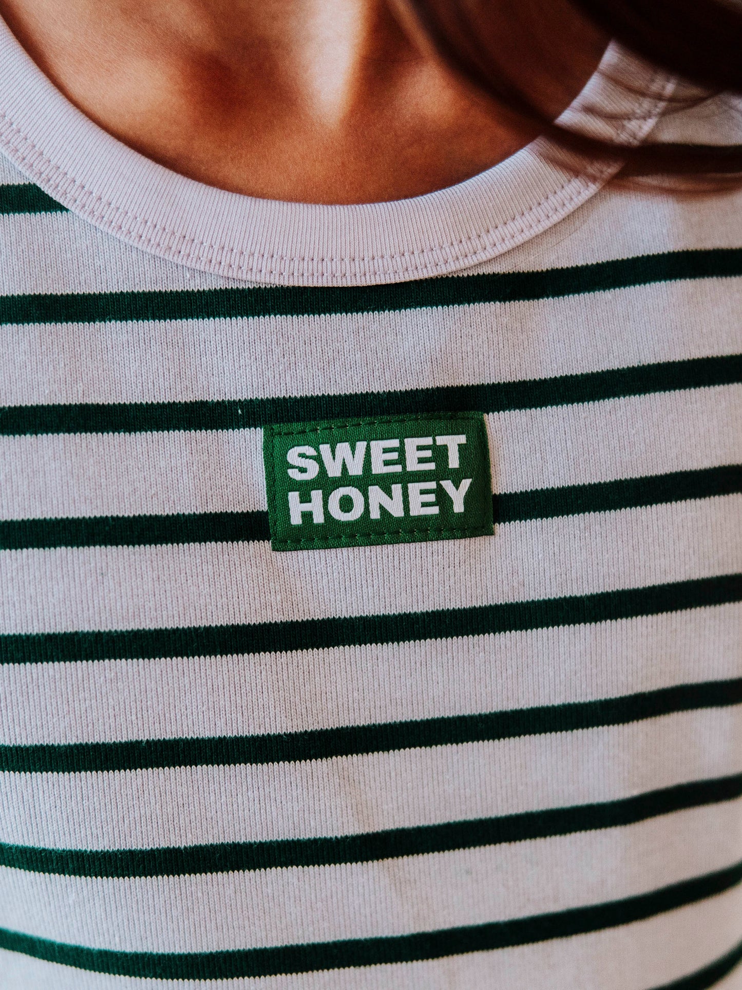 Up close shot of a SweetHoney logo tag that is green and white in color. Color of shirt is green and gray overall.