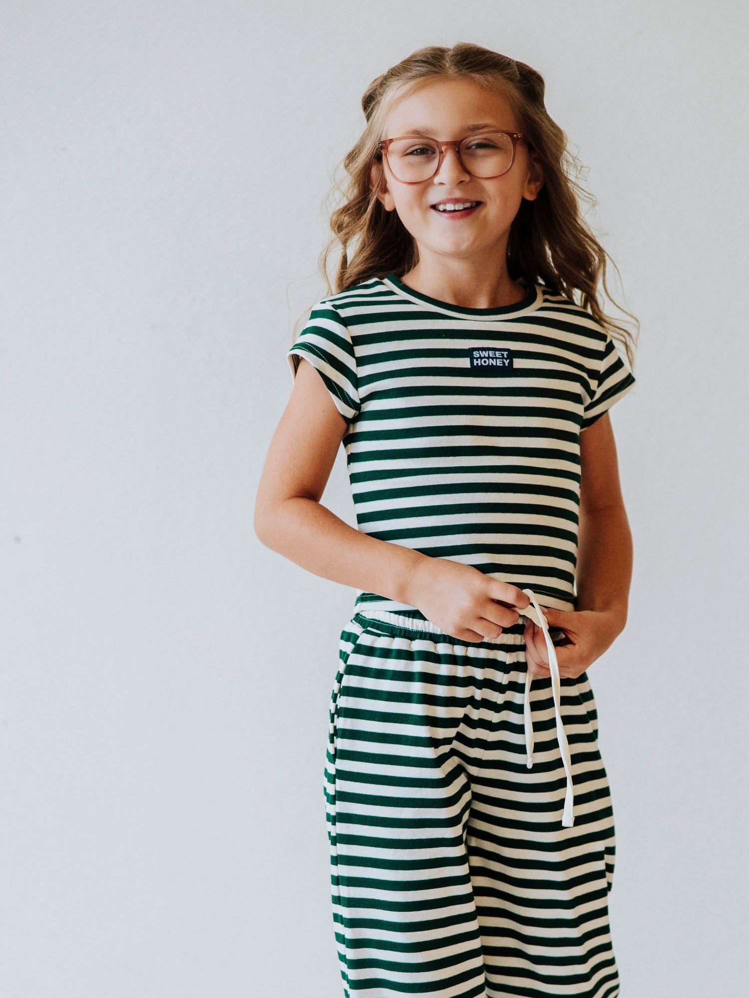 Girl is wearing a two-piece hunter green and ivory striped pant set. Girl is tying the drawstring on pants. 