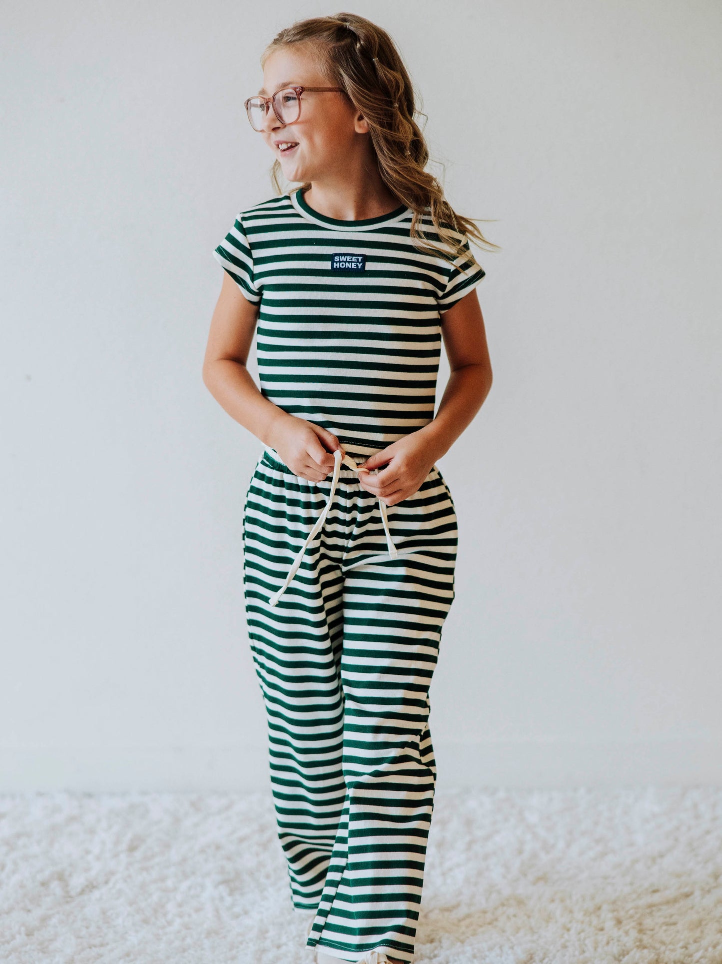 Girl is wearing a two-piece hunter green and ivory striped pant set. Girl is tying the drawstring on pants. 