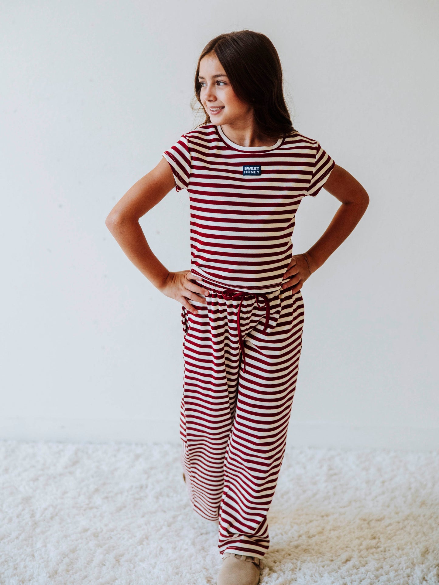 Girl is wearing a two-piece red and ivory striped pant set. Girl is wearing tan clogs and is posing. 