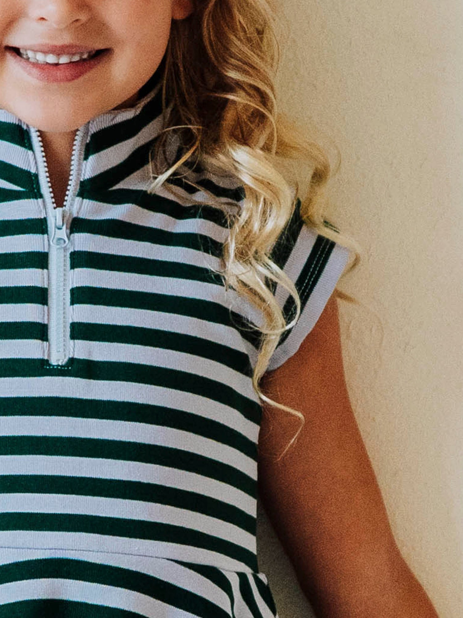 Up close picture of the cap sleeve and zipper closure on a green and gray colored garment. 