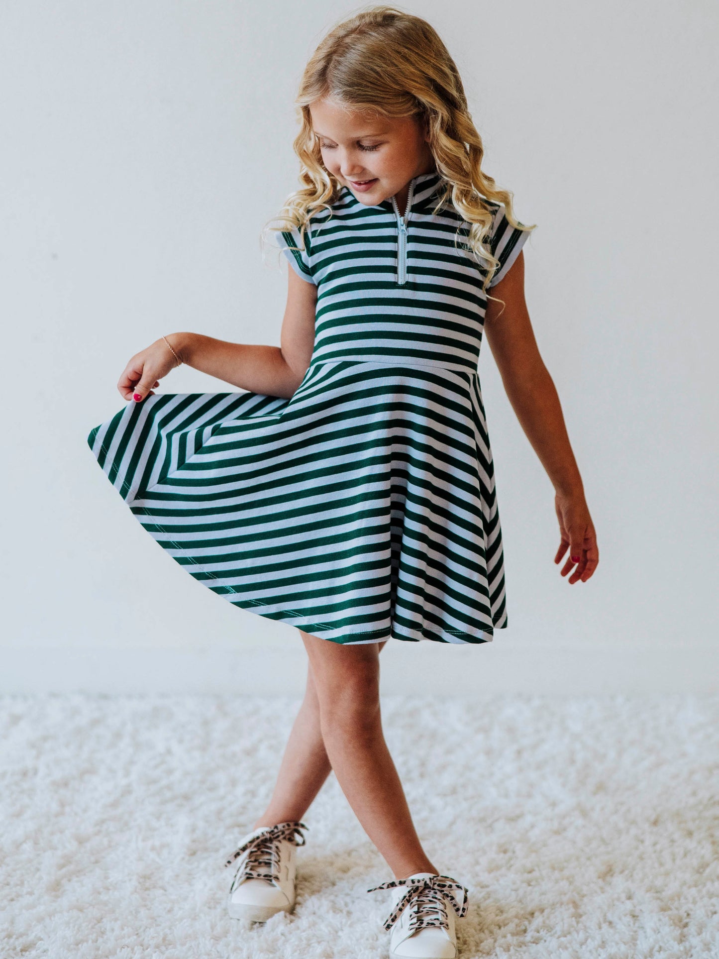 Model wearing a green and gray striped set with zipper closure at chest. Model is wearing white shoes. 