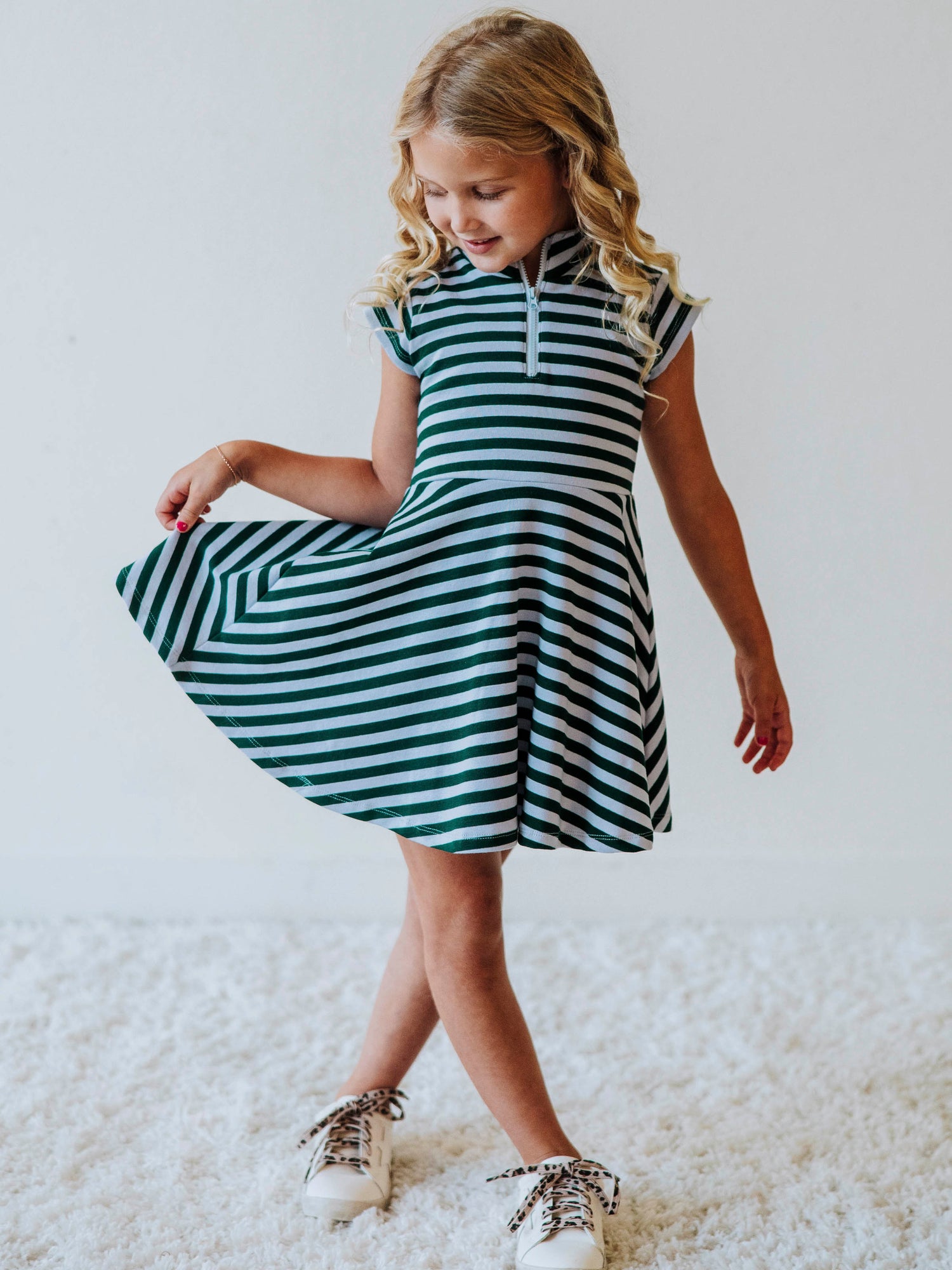Model wearing a green and gray striped set with zipper closure at chest. Model is wearing white shoes. 