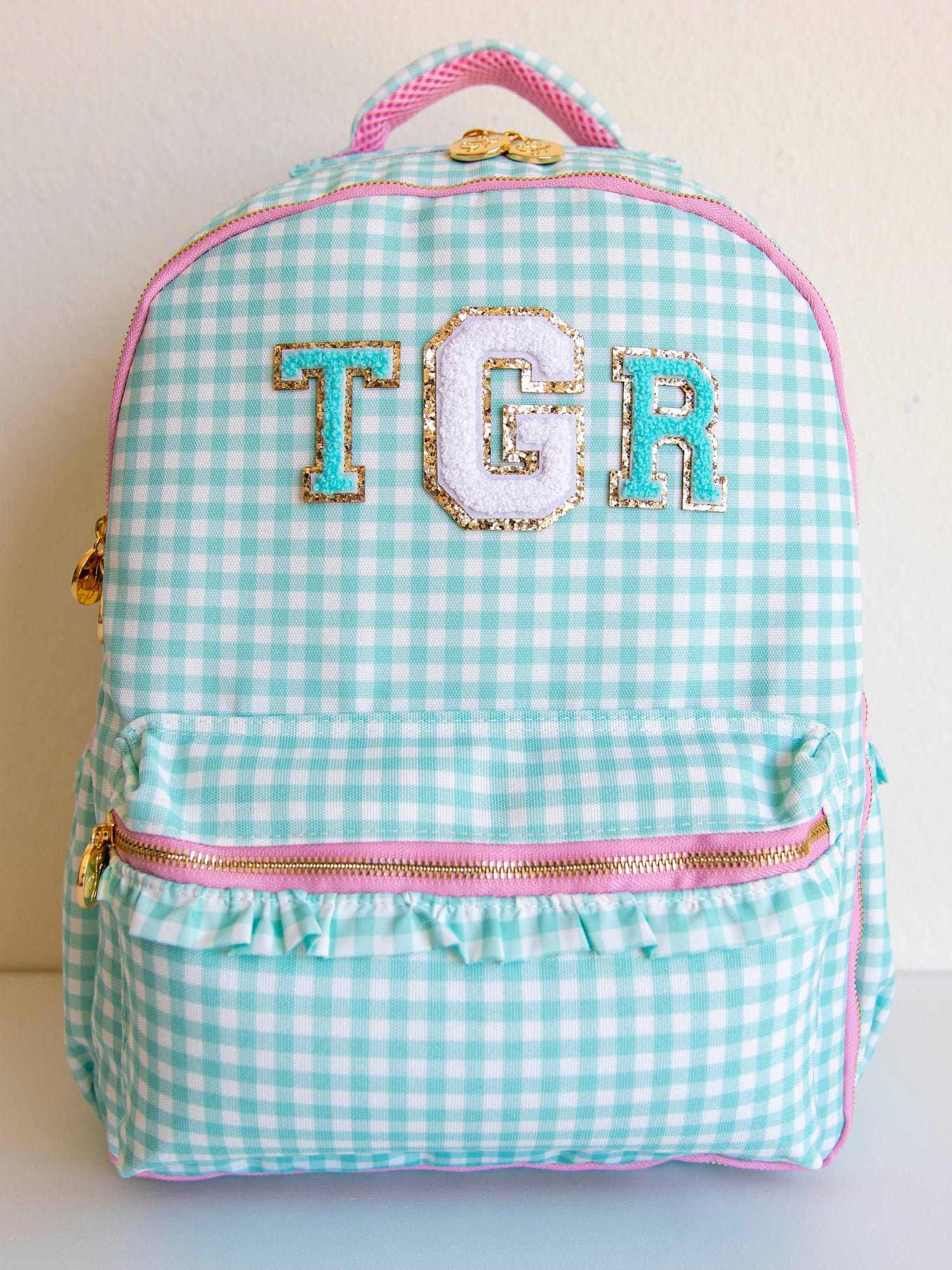 Mint green gingham backpack with pink zipper accents and gold zipper pulls. backpack shown with letter patches. 