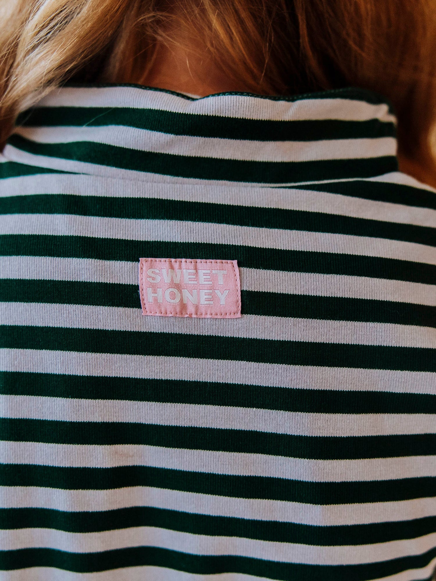 Close up shot of a Sweethoney stitched logo at back of green and gray dress. 
