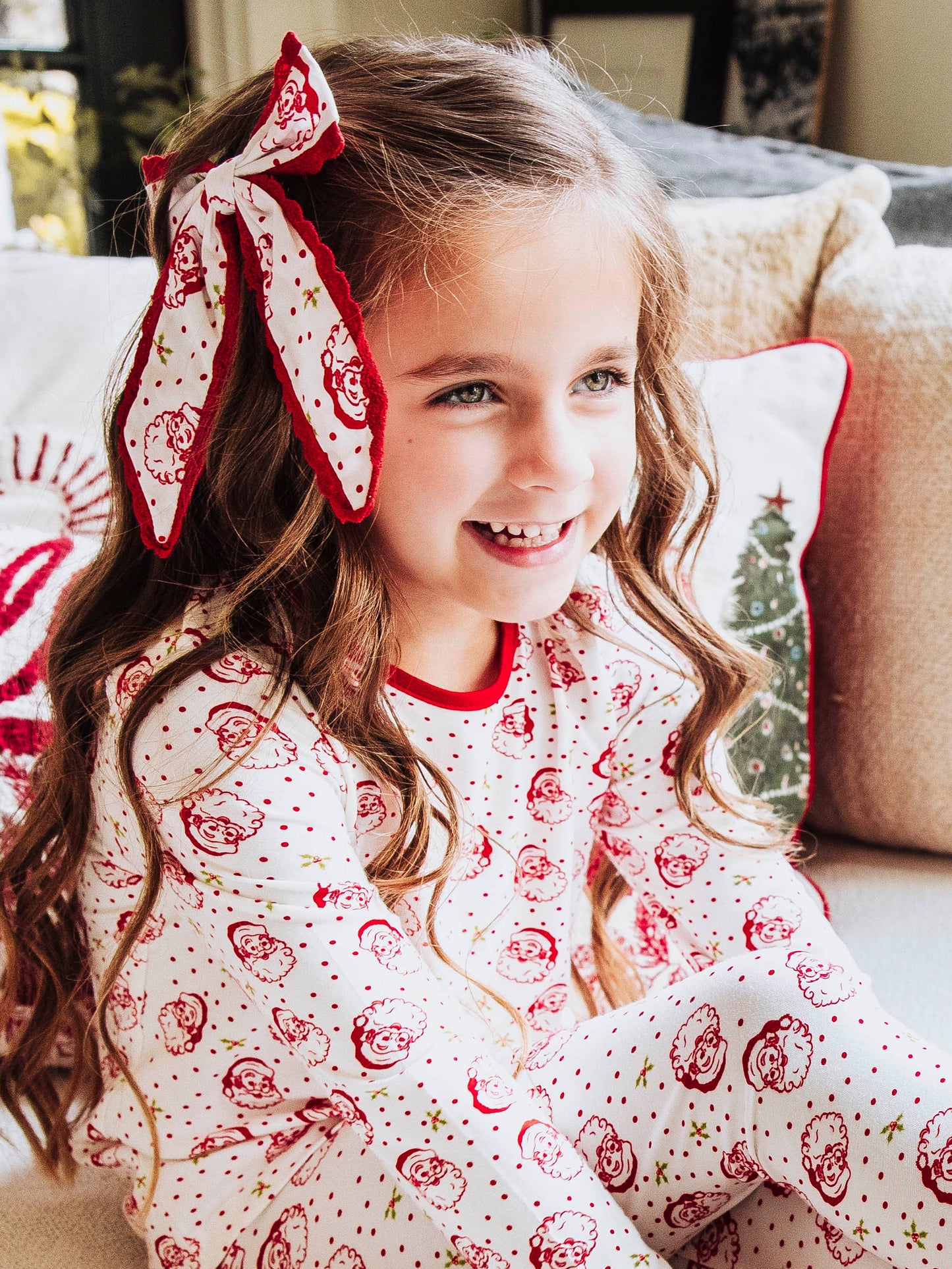 Model wearing a polka dot Santa bow trimmed in red and is wearing the same printed outfit.
