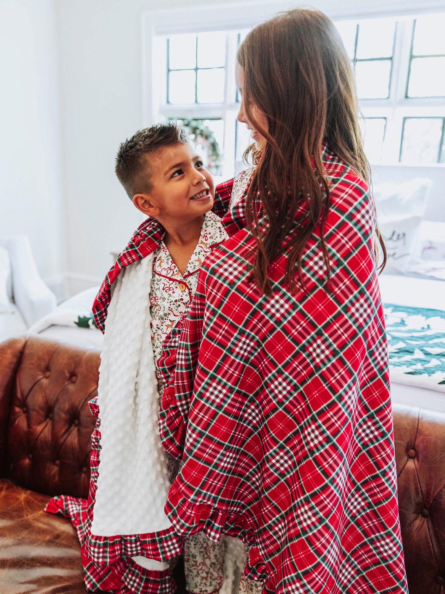 Boy and girl looking at one another. Both draped in a traditional Christmas plaid blanket. 
