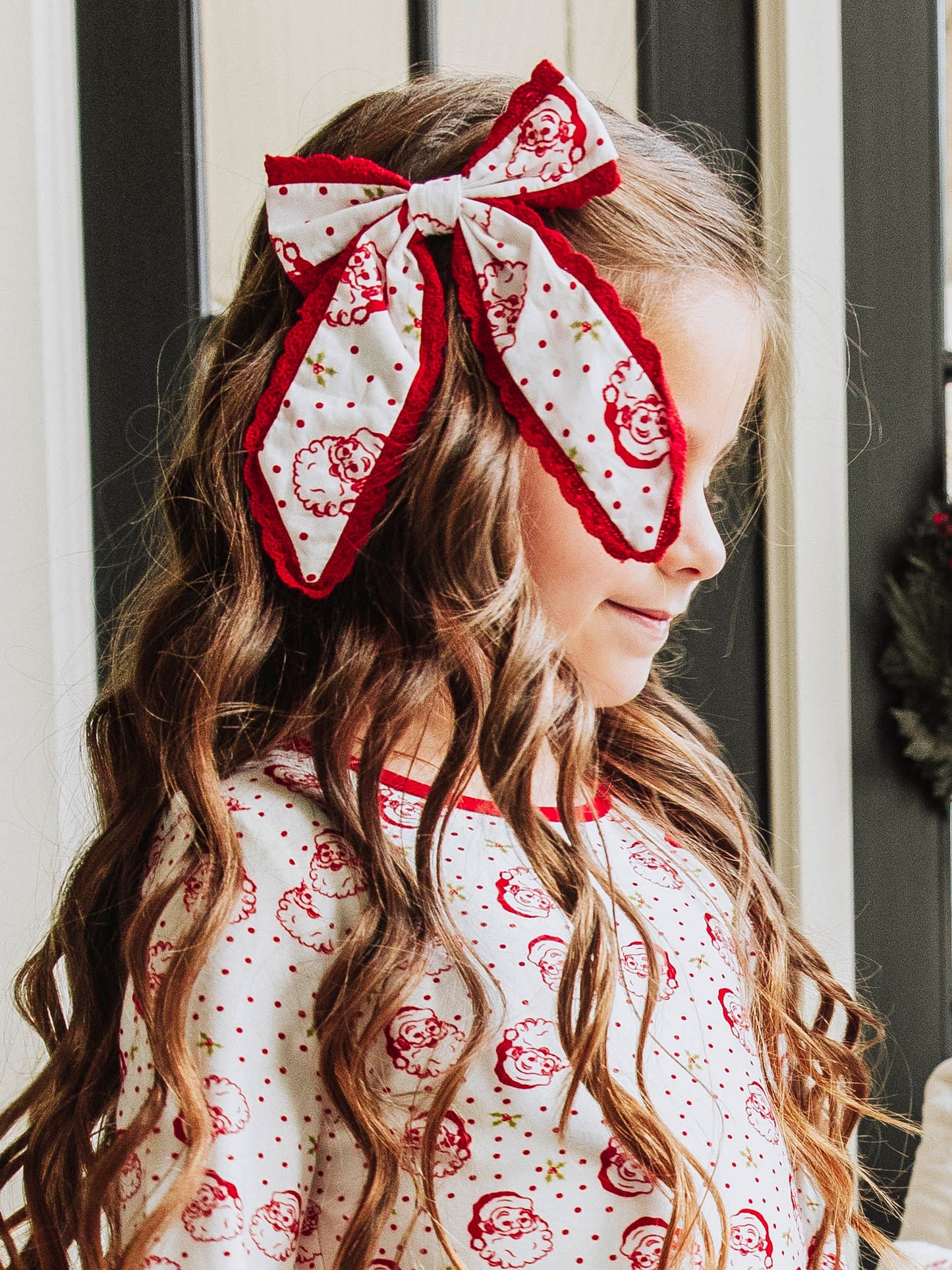 Model wearing a polka dot Santa bow trimmed in red and is wearing the same printed top. 