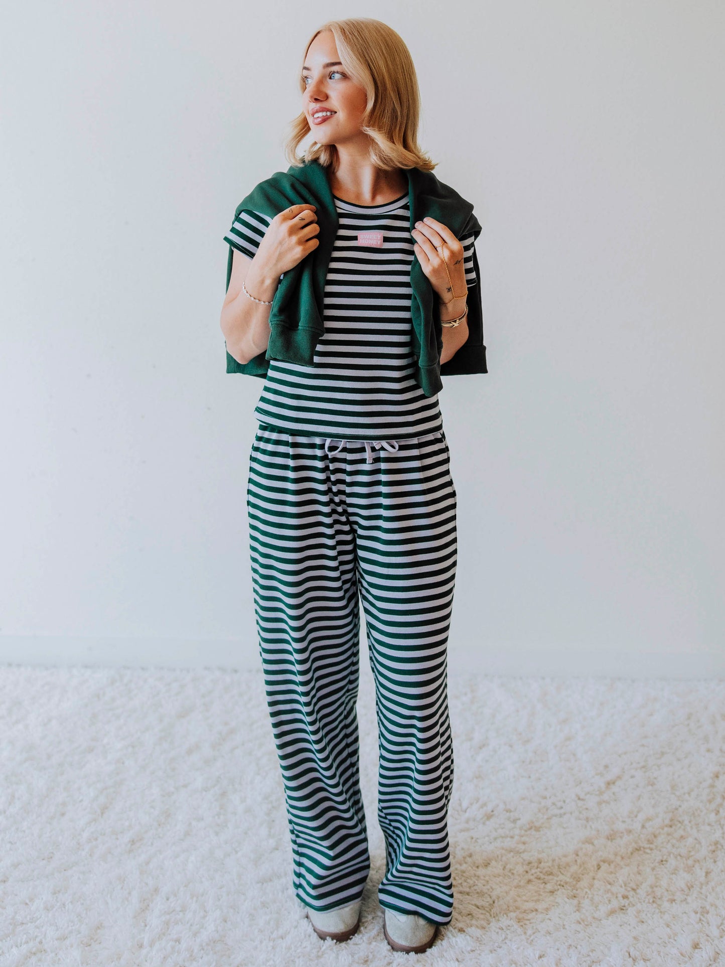 Model is wearing a green and lavender striped two-piece set with a green sweater draped over her shoulder. 