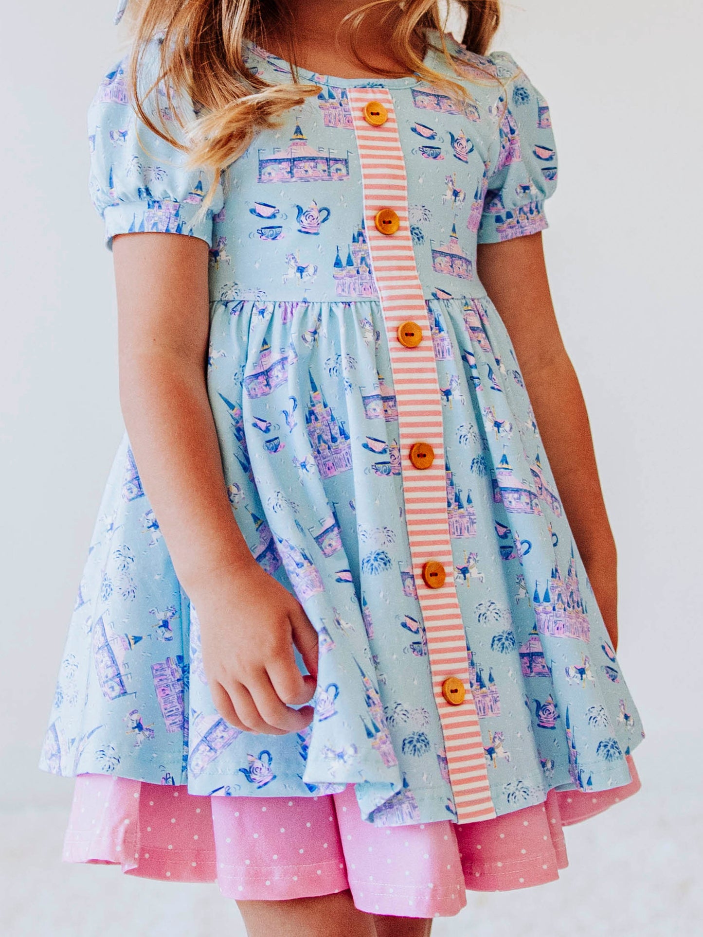 Bring a little fairytale charm to her day with our Most Magical Prim Dress! This enchanting dress features our exclusive Most Magical print — a whimsical pattern filled with castles, teacups, and dreamy pastel details. Designed with a sweet button-down front, short puff sleeves, and a full twirl skirt trimmed in pink polka dots, it’s perfect for playdates, park adventures, and magical memories.