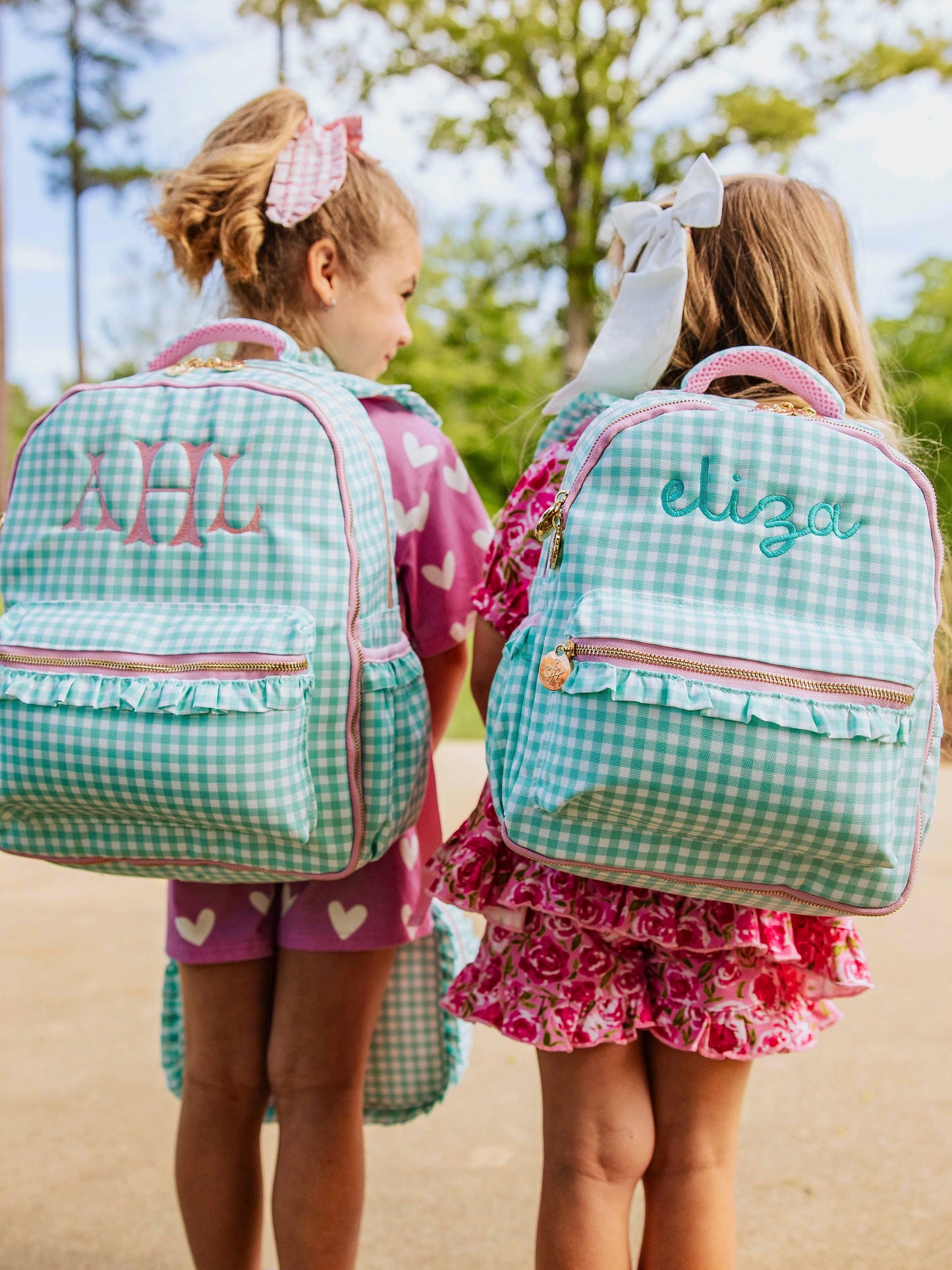 Two girls outside wearing mint green gingham backpacks both with custom embroidery. 