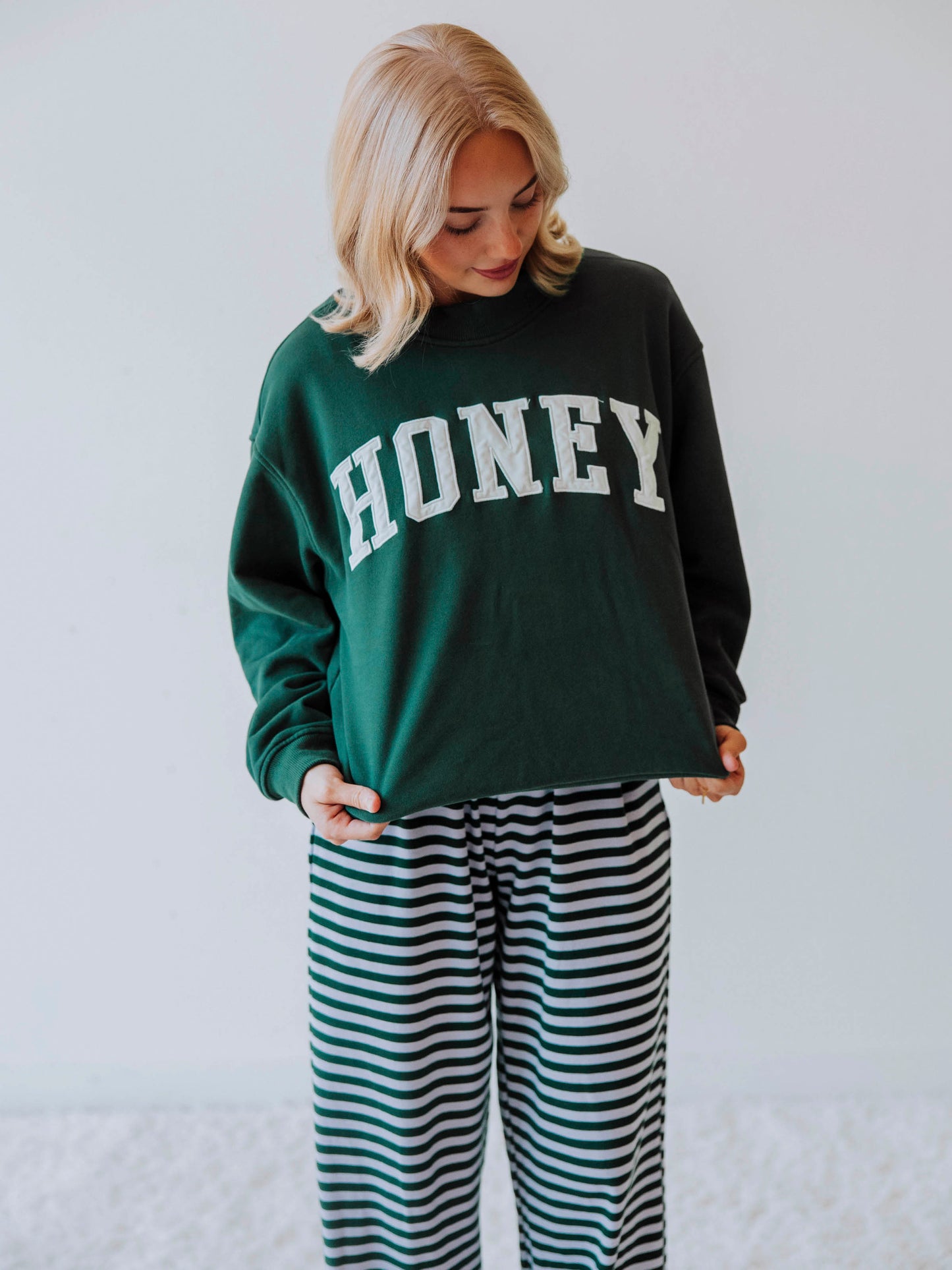 Girl wearing a green mock neck sweatshirt  that says HONEY on the front. Bottoms appear to be striped.