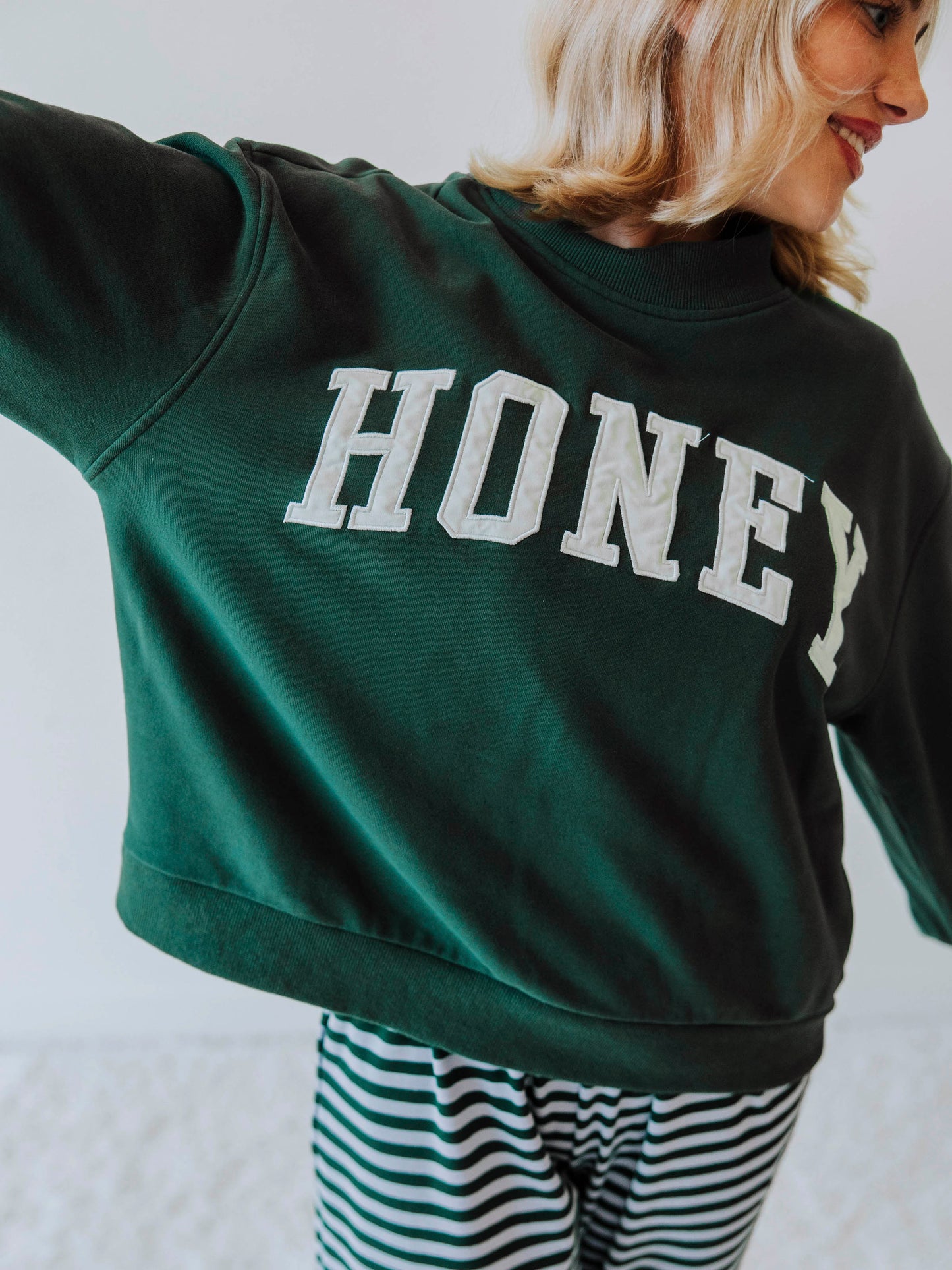Girl wearing a green mock neck sweatshirt  that says HONEY on the front. Bottoms appear to be striped.