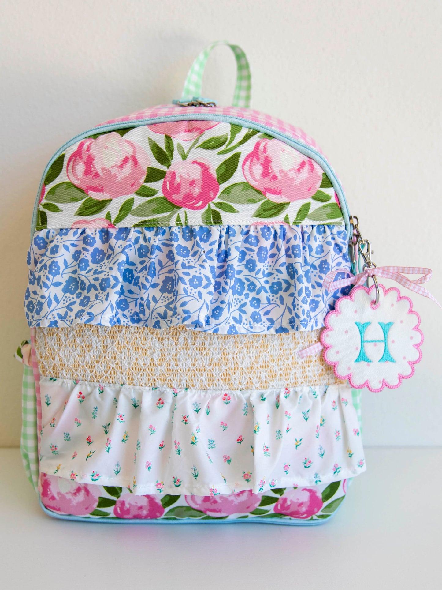 colorful and floral backpack with drape ruffle detail. On the side, there is a customized embroidery tag.
