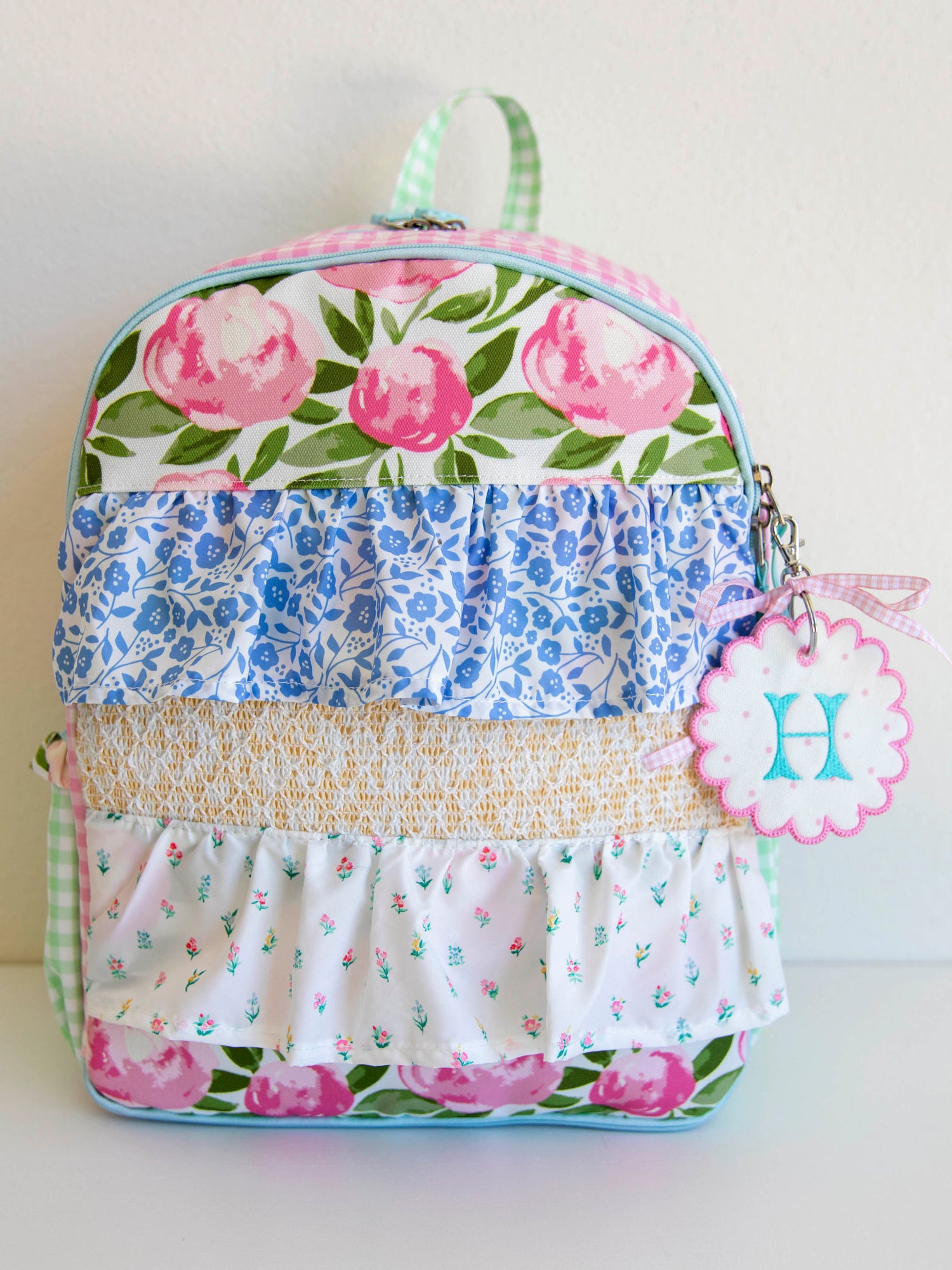 colorful and floral backpack with drape ruffle detail. On the side, there is a customized embroidery tag.