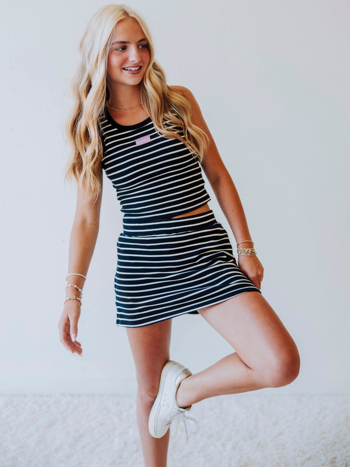 Model wearing a navy and white striped skort set. Top has a Sweethoney stitched logo tag in the middle of chest and model has one foot propeed on the inside of knee.
