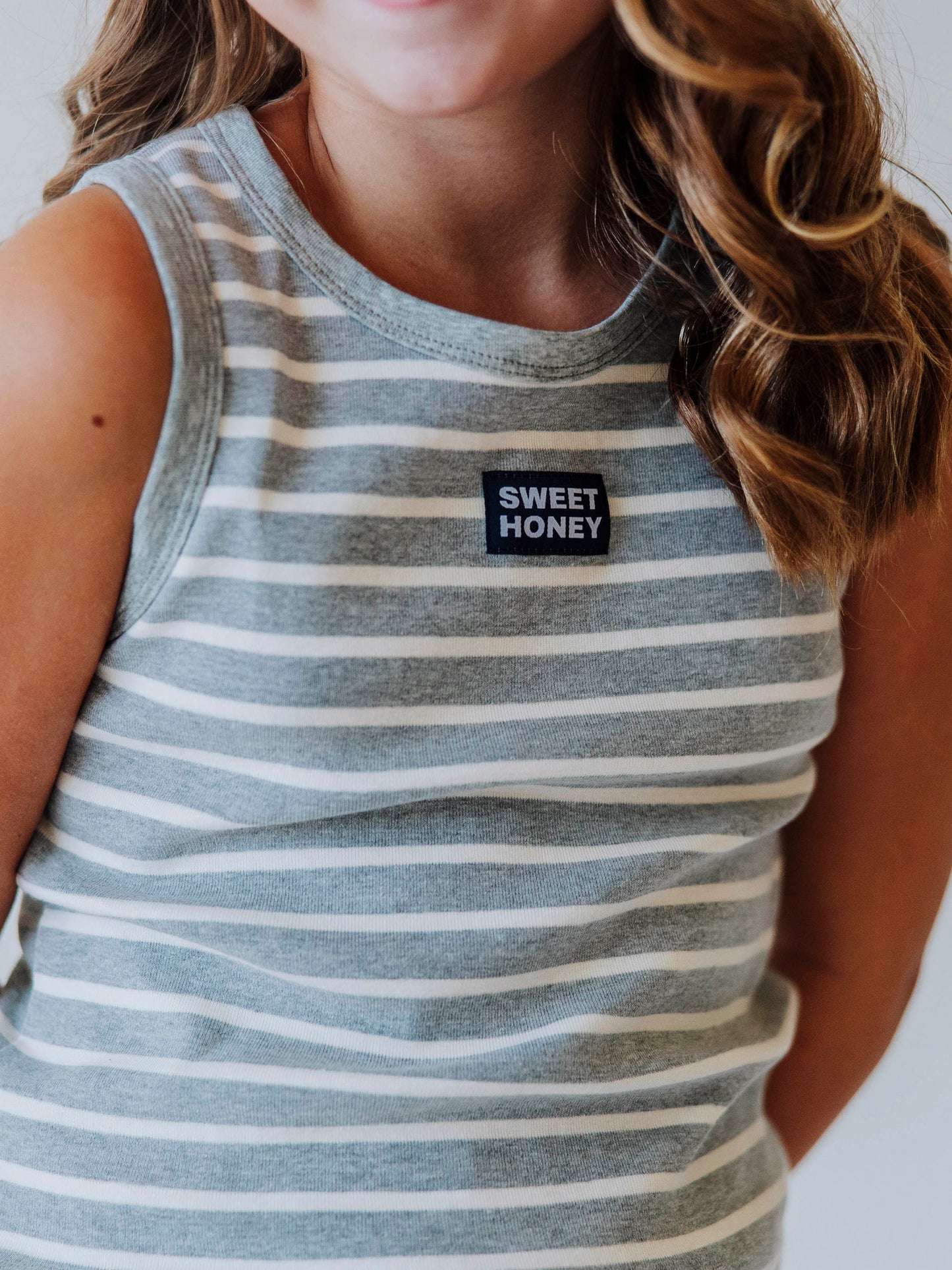 Model is wearing a two-piece gray and white striped skort set. There is a SweetHoney tag that is centered on front of shirt and is navy and white in color. t. 
