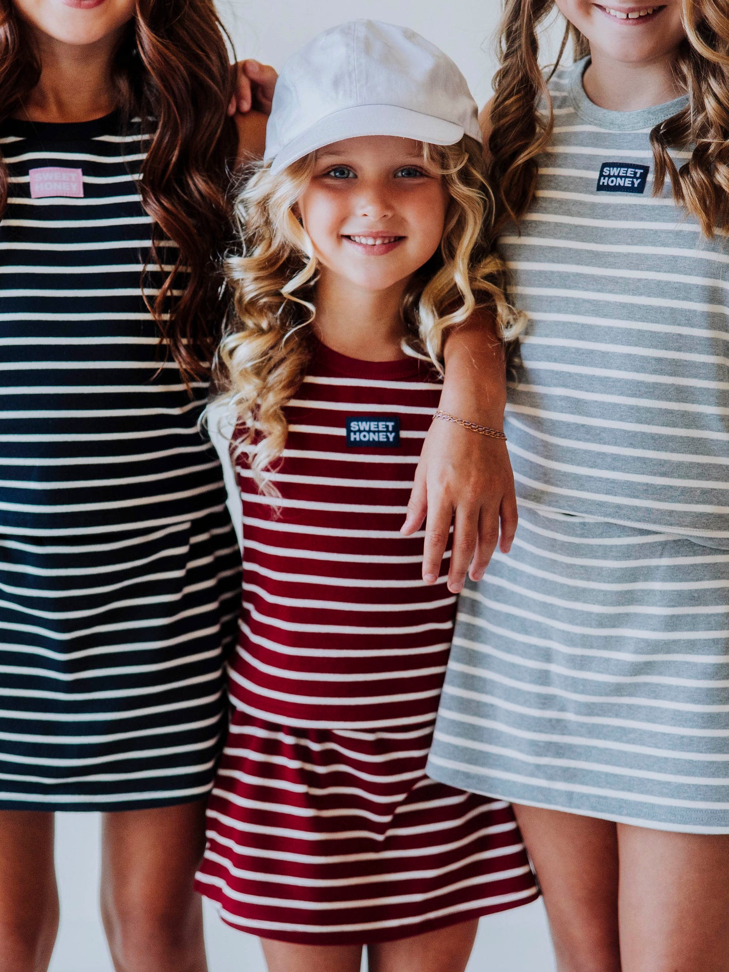 Set of three models all posing and wearing two piece skort sets. One is navy stripe, middle is crimson and ivory stripe, and model on the right is gray and white stripe. 