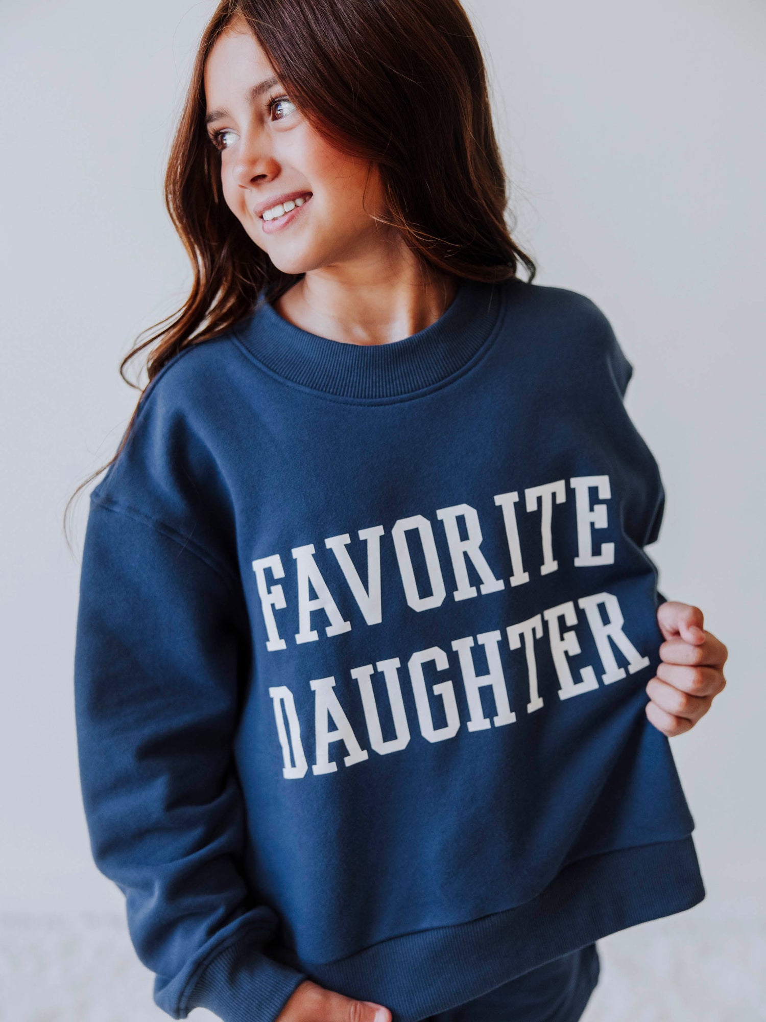 Model is wearing a two piece, navy sweat set that has FAVORITE DAUGHTER on the front in white vinyl letters. 