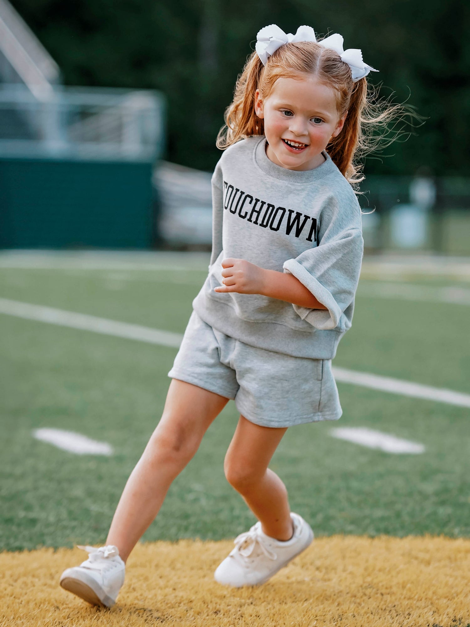 Girl wearing a gray two-piece set that says TOUCHDOWN in black writing on front. Girl appears to be running. 