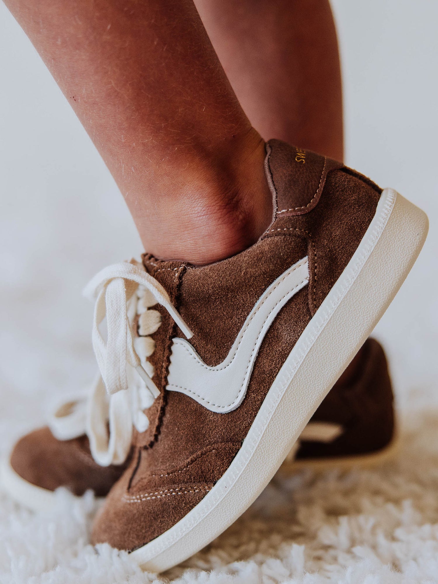 Brown mocha colored suede sneakers with a swish design on the side in a creamy white and creamy white laces.