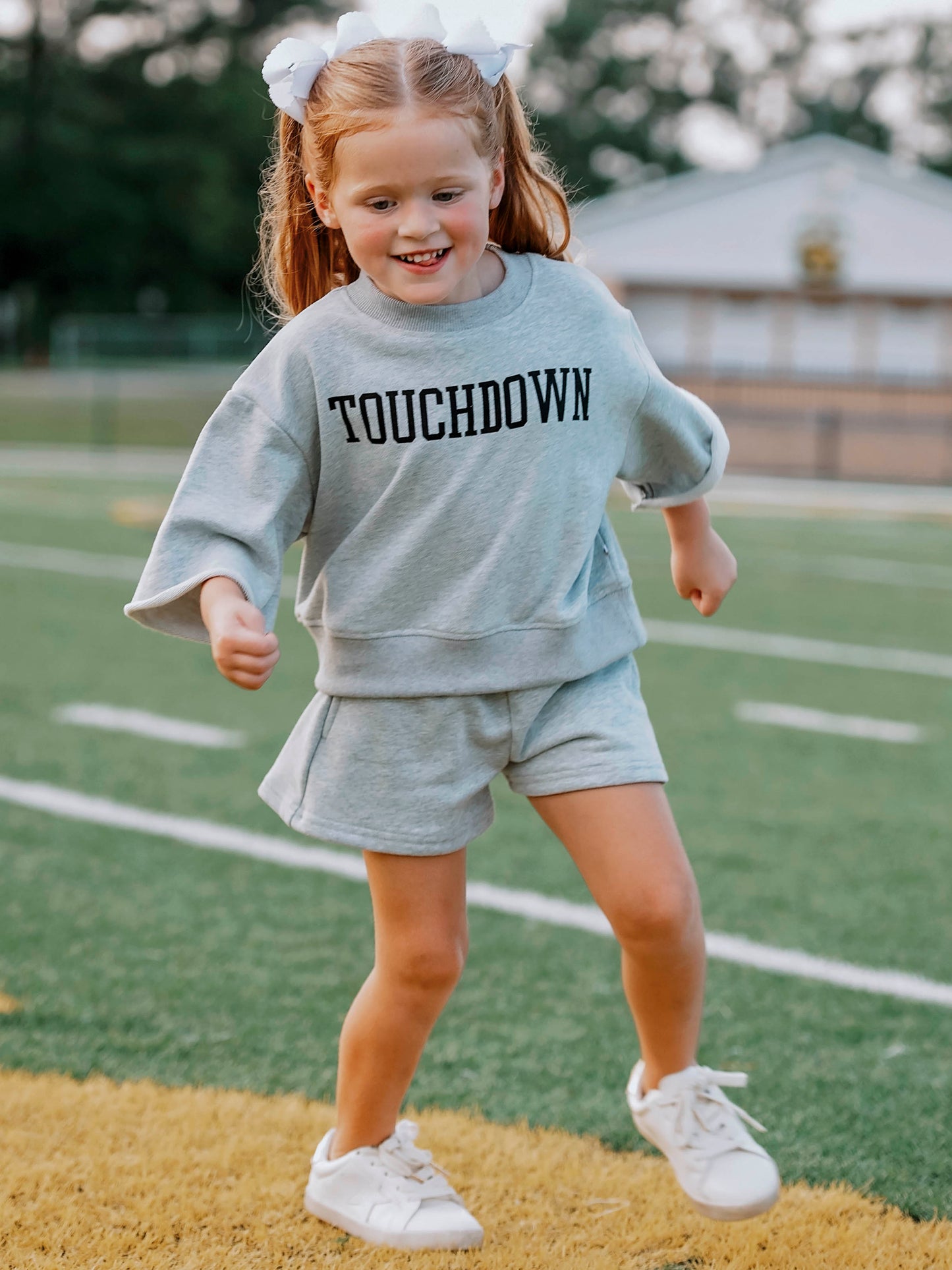 Girl wearing a gray two-piece set that says TOUCHDOWN in black writing on front. Girl appears to be running. 