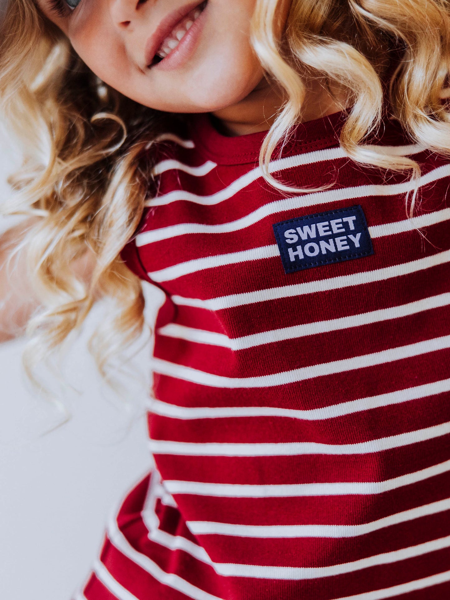 Model is wearing a two-piece, crimson and ivory striped skort set. Model is wearing a white hat. Centered on the shirt is a SweetHoney tag that is navy and white in color. 