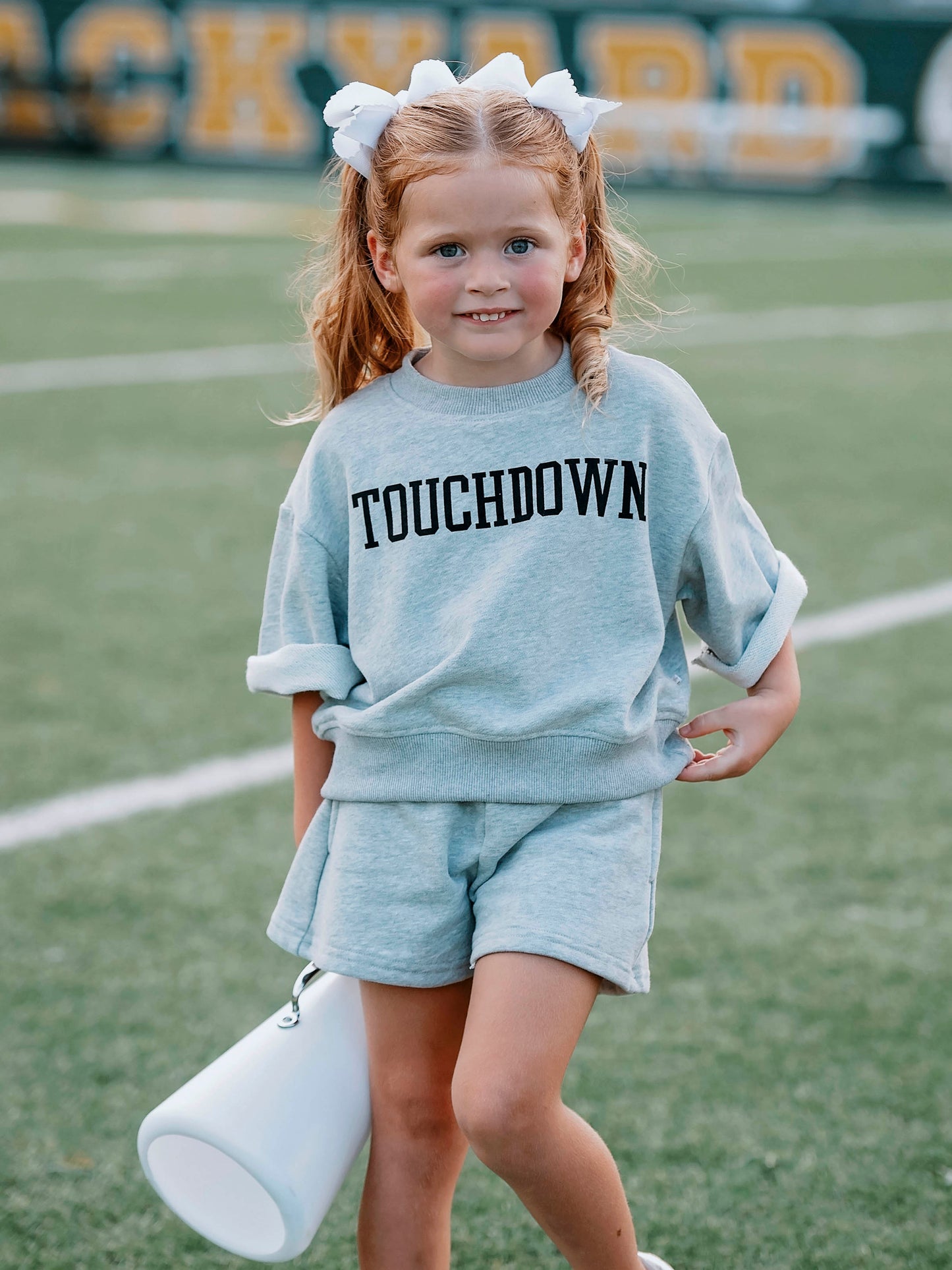 Girl wearing a gray two-piece set that says TOUCHDOWN in black writing on front. 