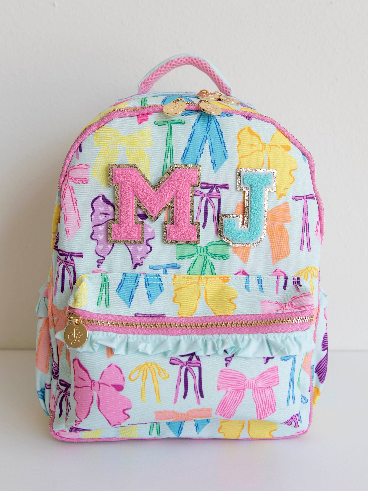 Vibrant bows printed backpack with different colored letter patches with, gold zippers and zipper pulls, and a handle