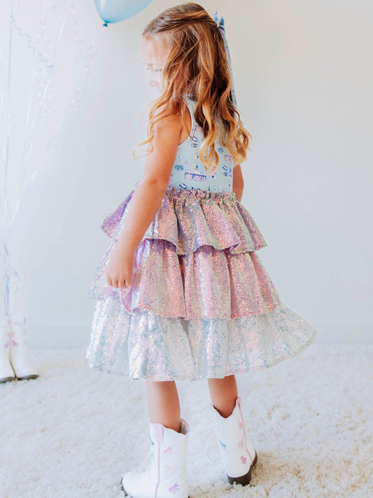 Make every day feel like a fairytale in our Most Magical Tiered Sparkle Dress! This enchanting girls’ dress features our signature “Most Magical” print bodice — filled with dreamy castles, carousels, and whimsical details — paired with a tiered iridescent sequin skirt that shimmers with every twirl. Designed for comfort and style, it’s perfect for holiday photos, birthday parties, or any moment that calls for a little extra sparkle. The soft lining ensures an itch-free fit, while the sleeveless design makes