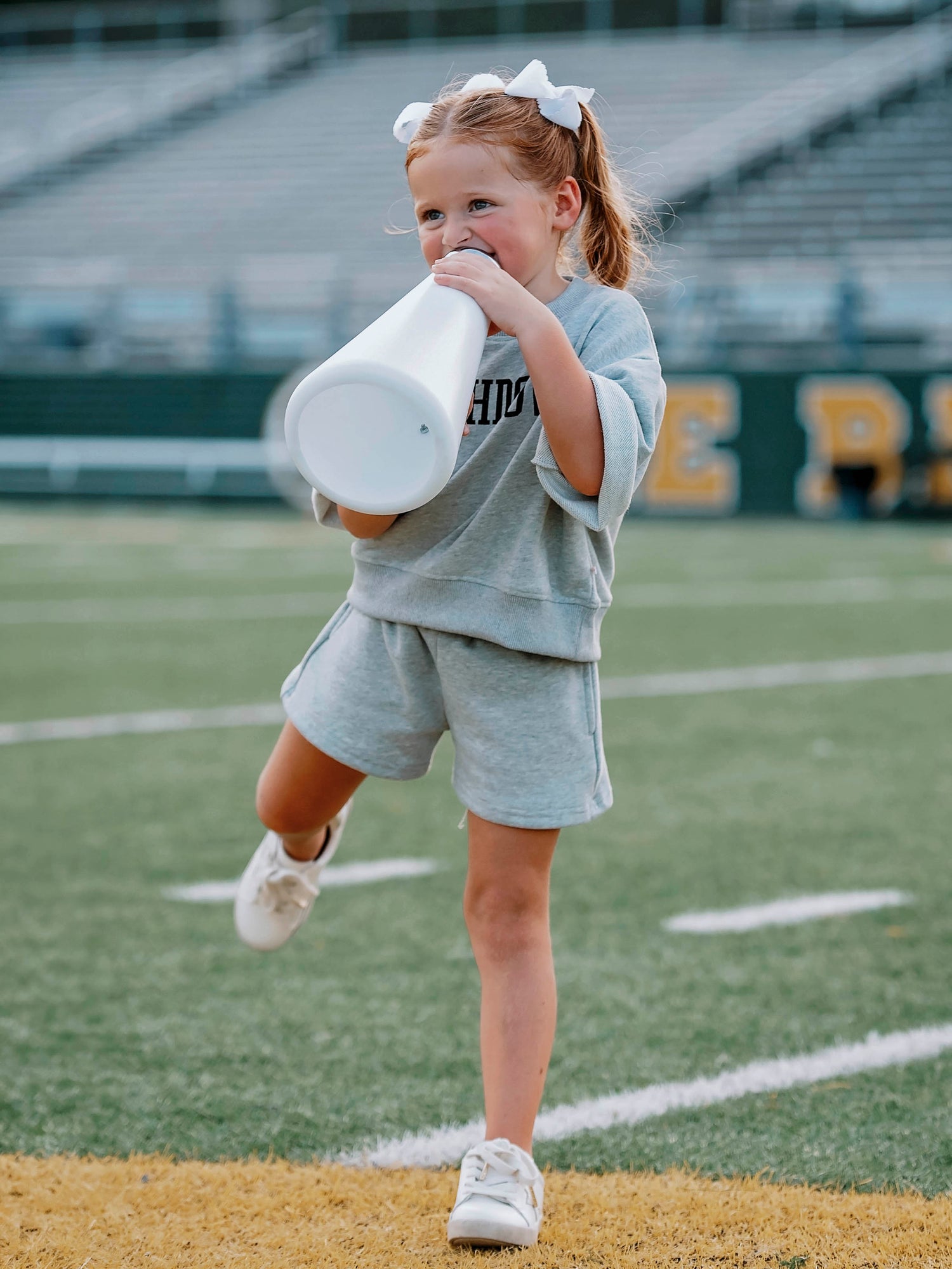 Girl wearing a gray two-piece set that says TOUCHDOWN in black writing on front. Girl appears to be running. 