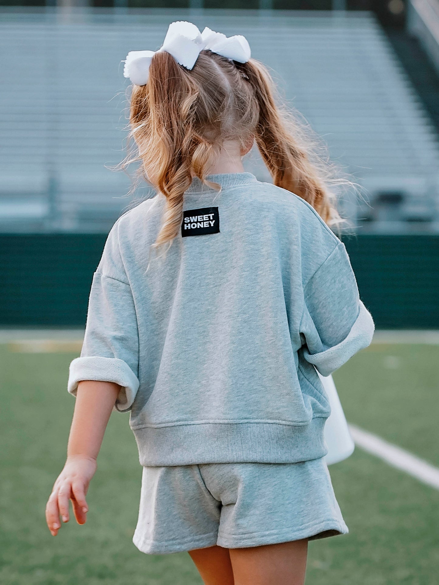 Backside of girl wearing a gray two piece set. Picture shows a SWEETHONEY logo tag at top of back