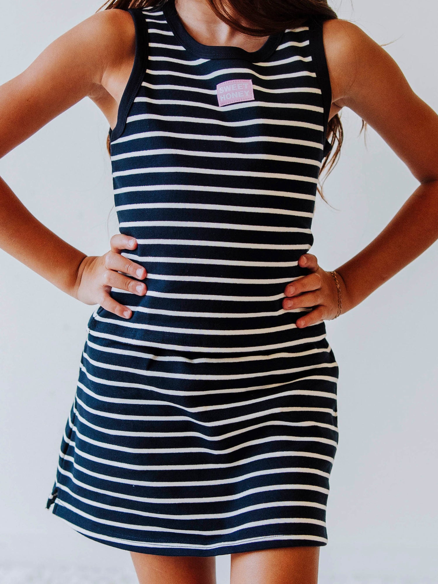 Model wearing a two-piece navy and cream striped skort set. There is a pink and white stitched SweetHoney tag in the middle of shirt. 