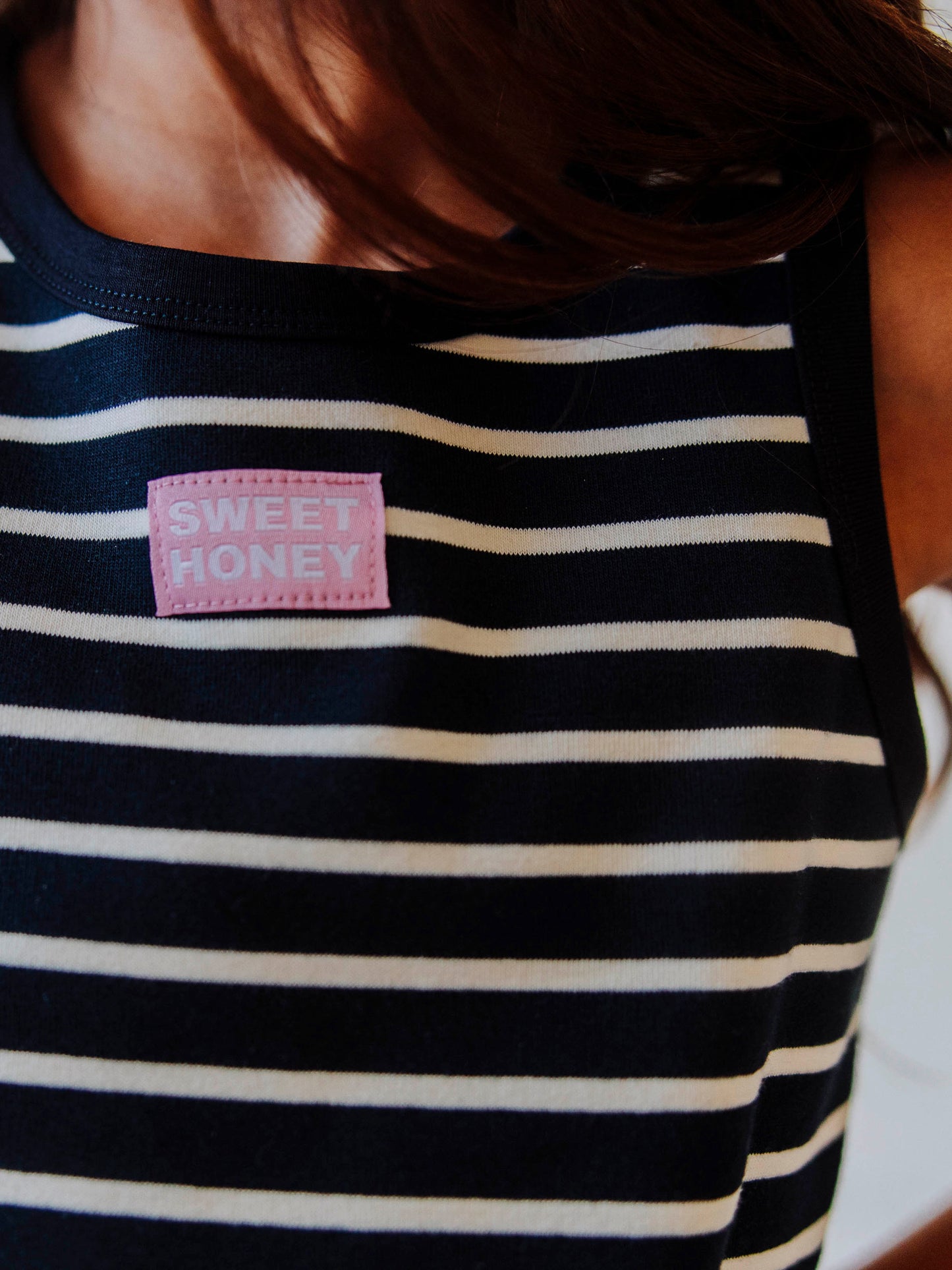 Up close picture of a navy and ivory striped shirt. There is a SweetHoney stitched tag in the middle of shirt. 