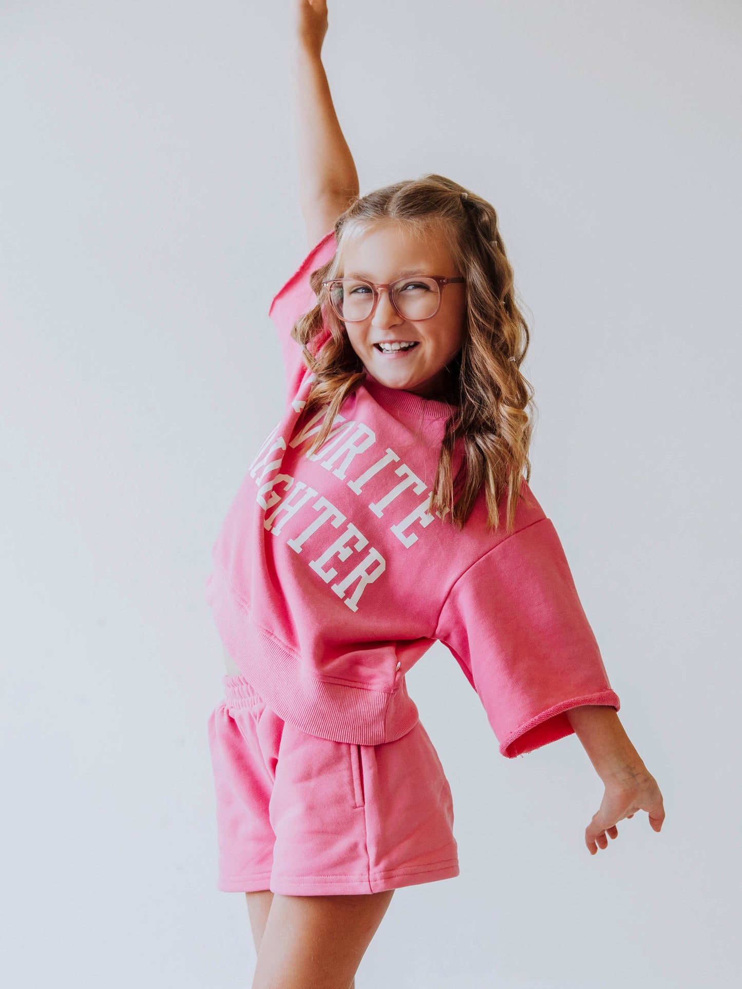 Model is wearing a two-piece, pink sweat set that has bell hemmed sleeves and the top has FAVORITE DAUGHTER in white vinyl lettering. 