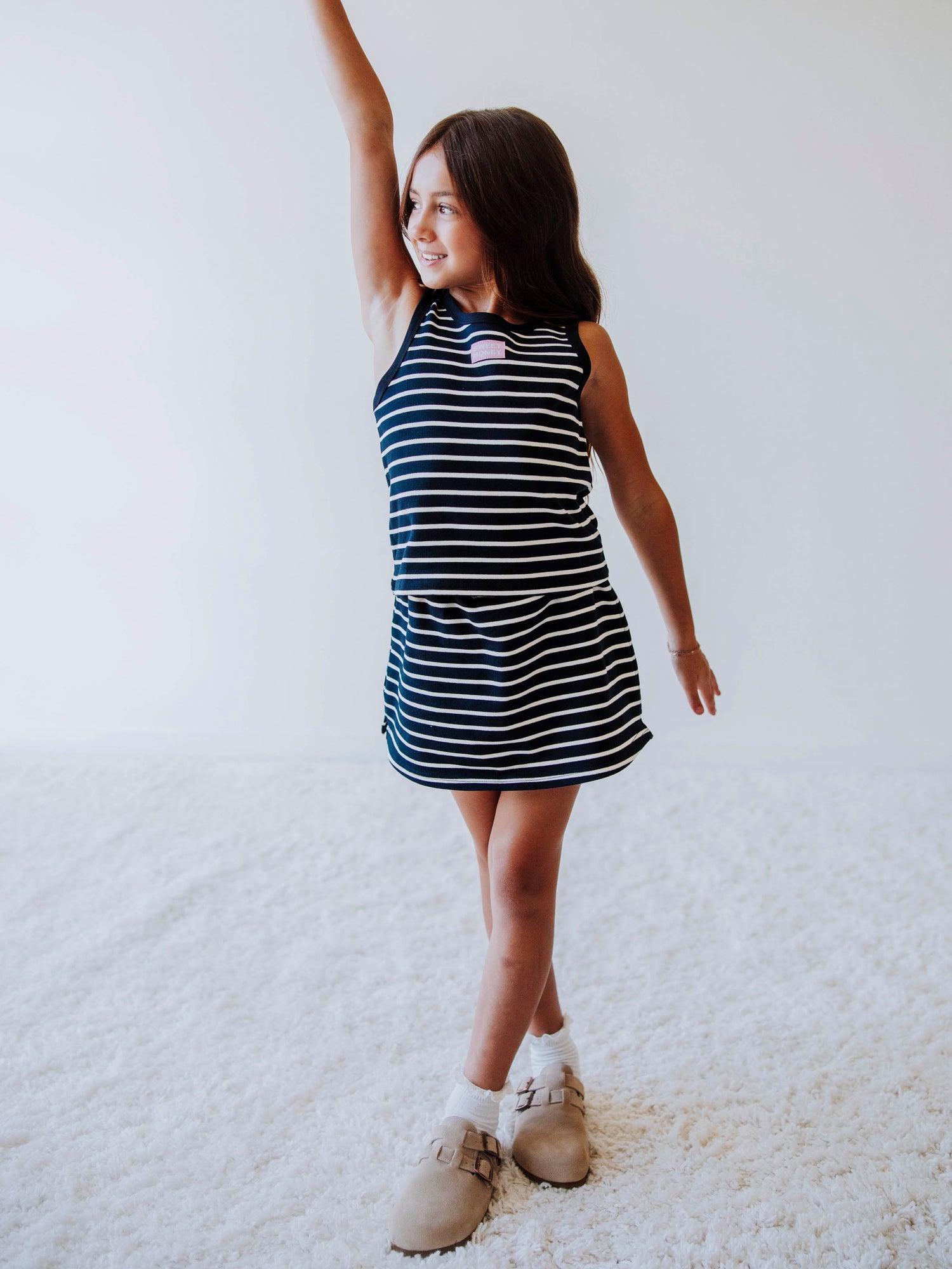 Model wearing a two-piece navy and cream striped skort set. Model is posing and is wearing clogs. Model is posing. 
