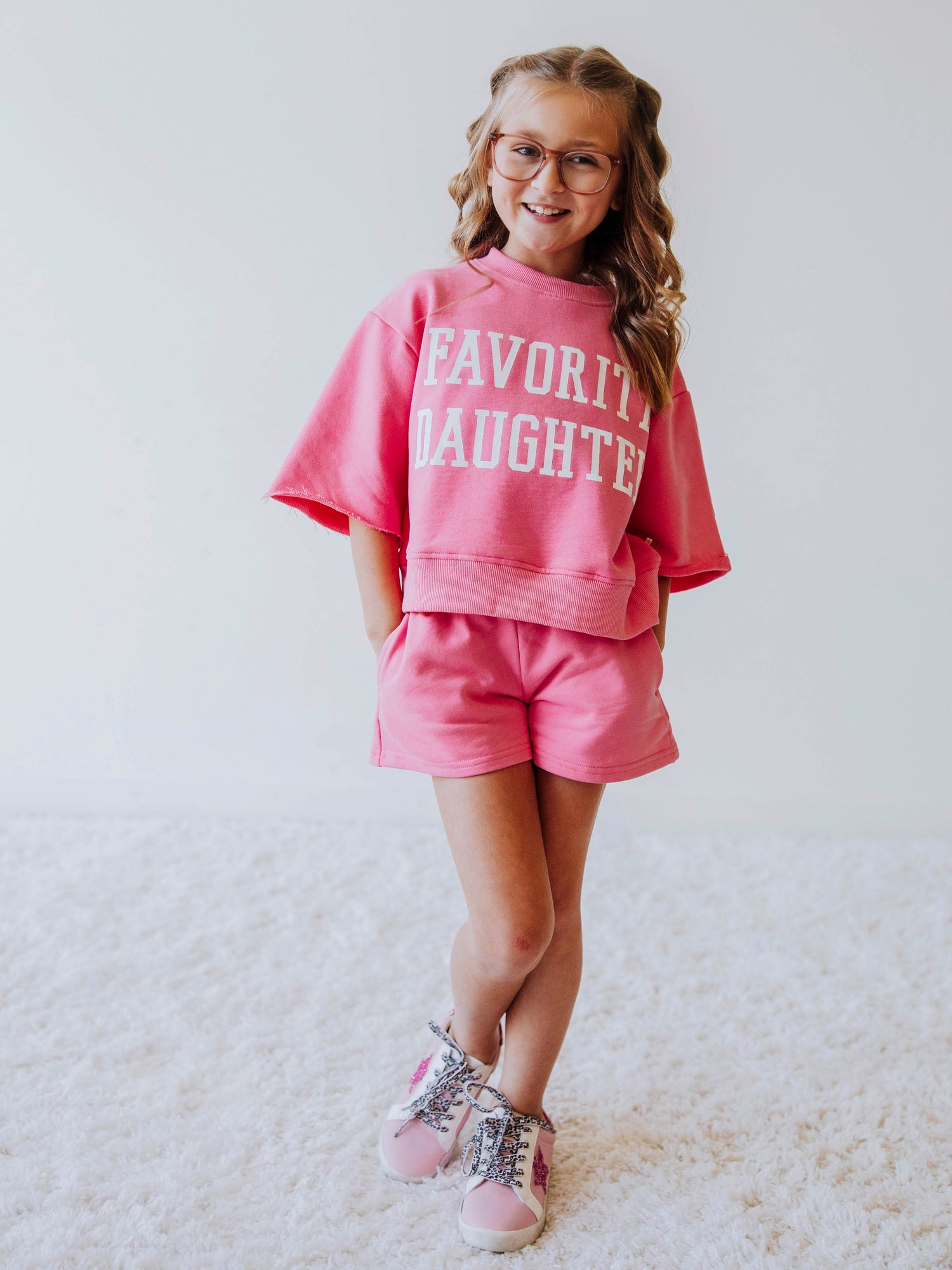 Model is wearing a two-piece, pink sweat set that has bell hemmed sleeves and the top has FAVORITE DAUGHTER in white vinyl lettering. 