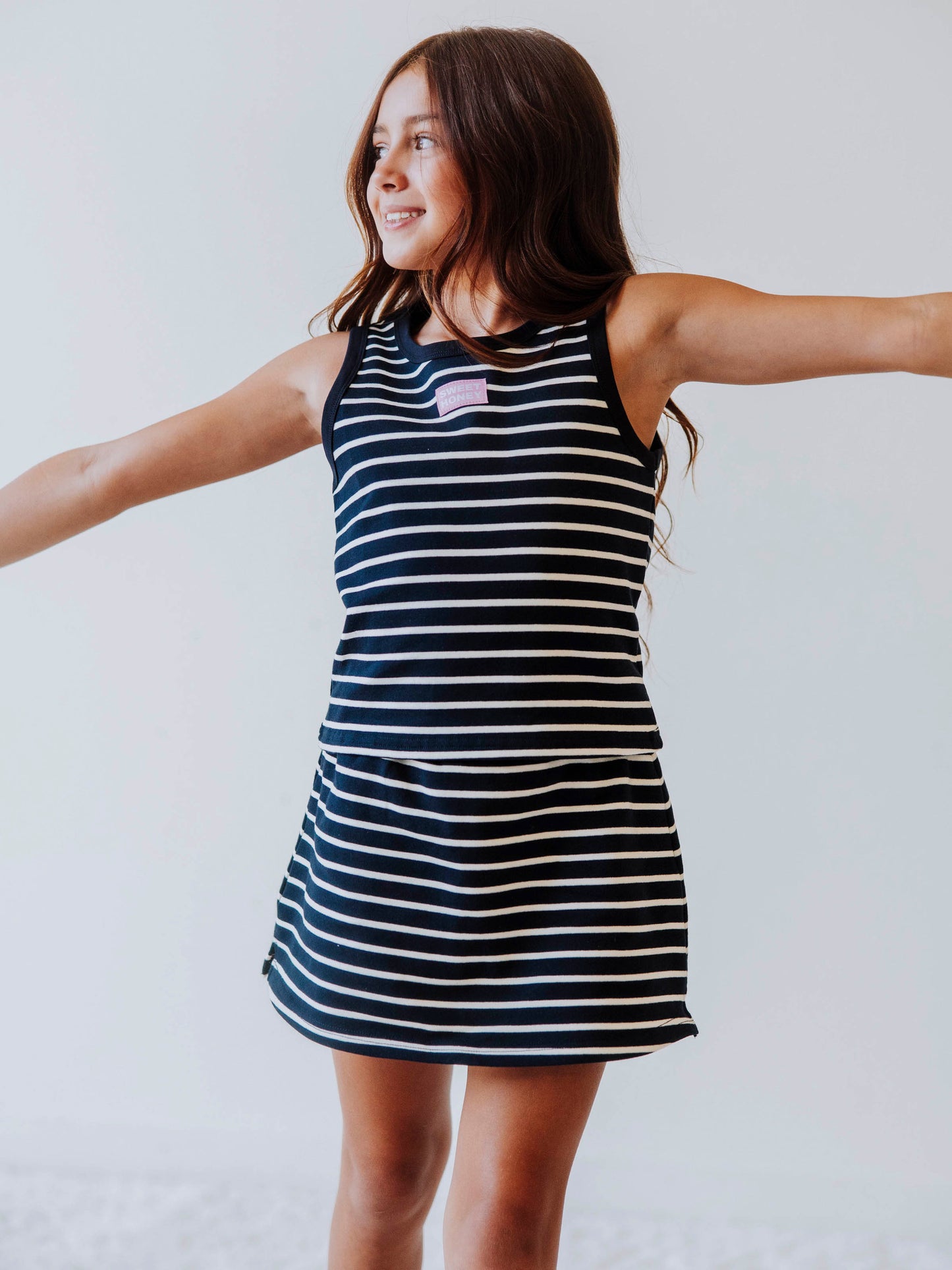 Model wearing a two-piece navy and cream striped skort set. There is a pink and white stitched SweetHoney logo tagged in the middle of chest. 