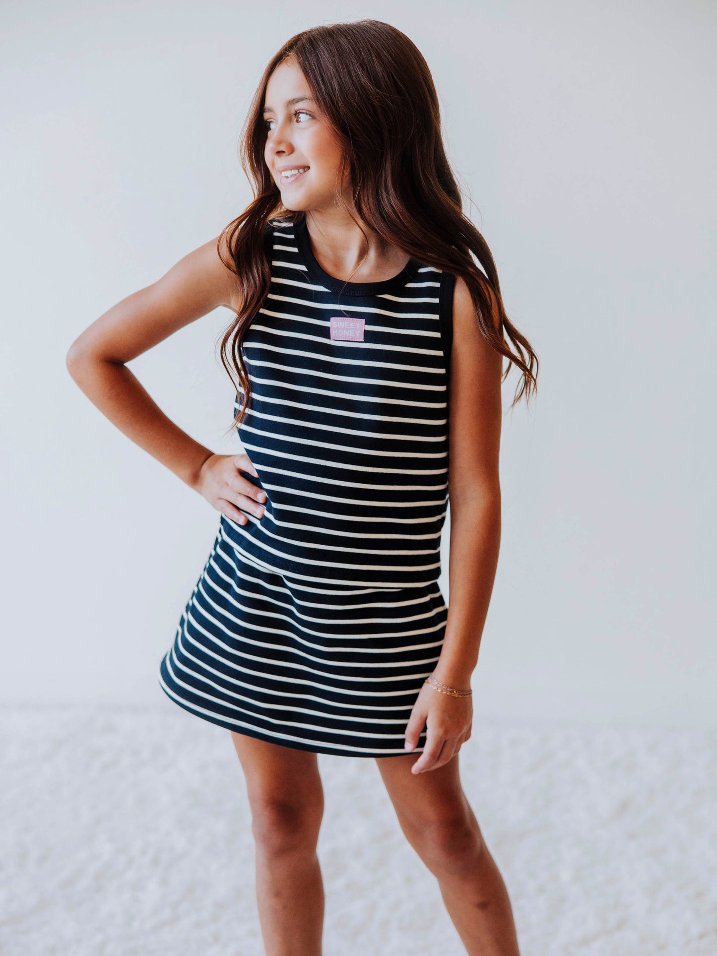 Model wearing a two-piece navy and cream striped skort set. There is a pink and white stitched SweetHoney tag in the middle of shirt. 