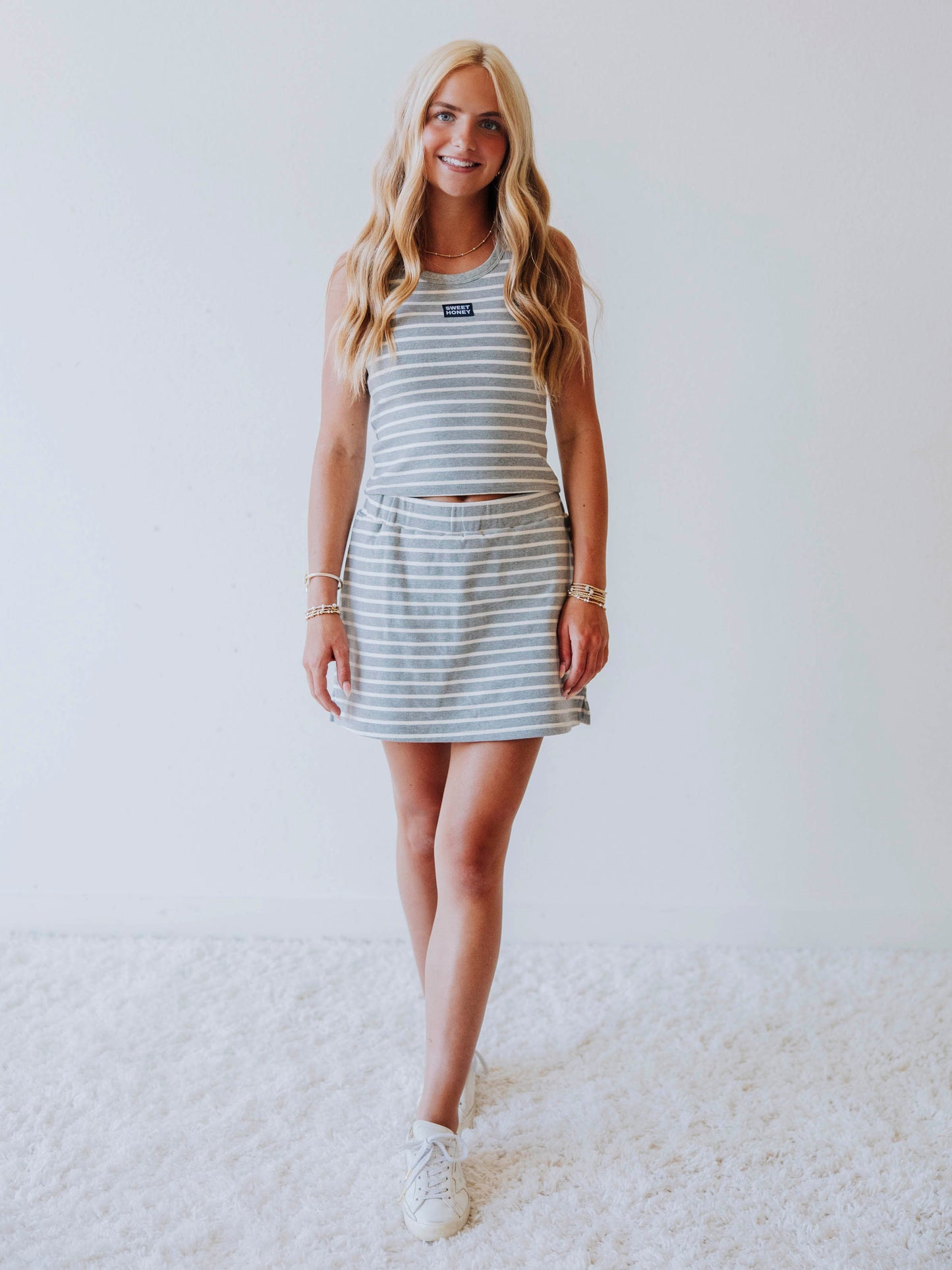Model wearing a gray and white stiped skort set. Top has a Sweethoney stitched logo tag in the middle of chest
