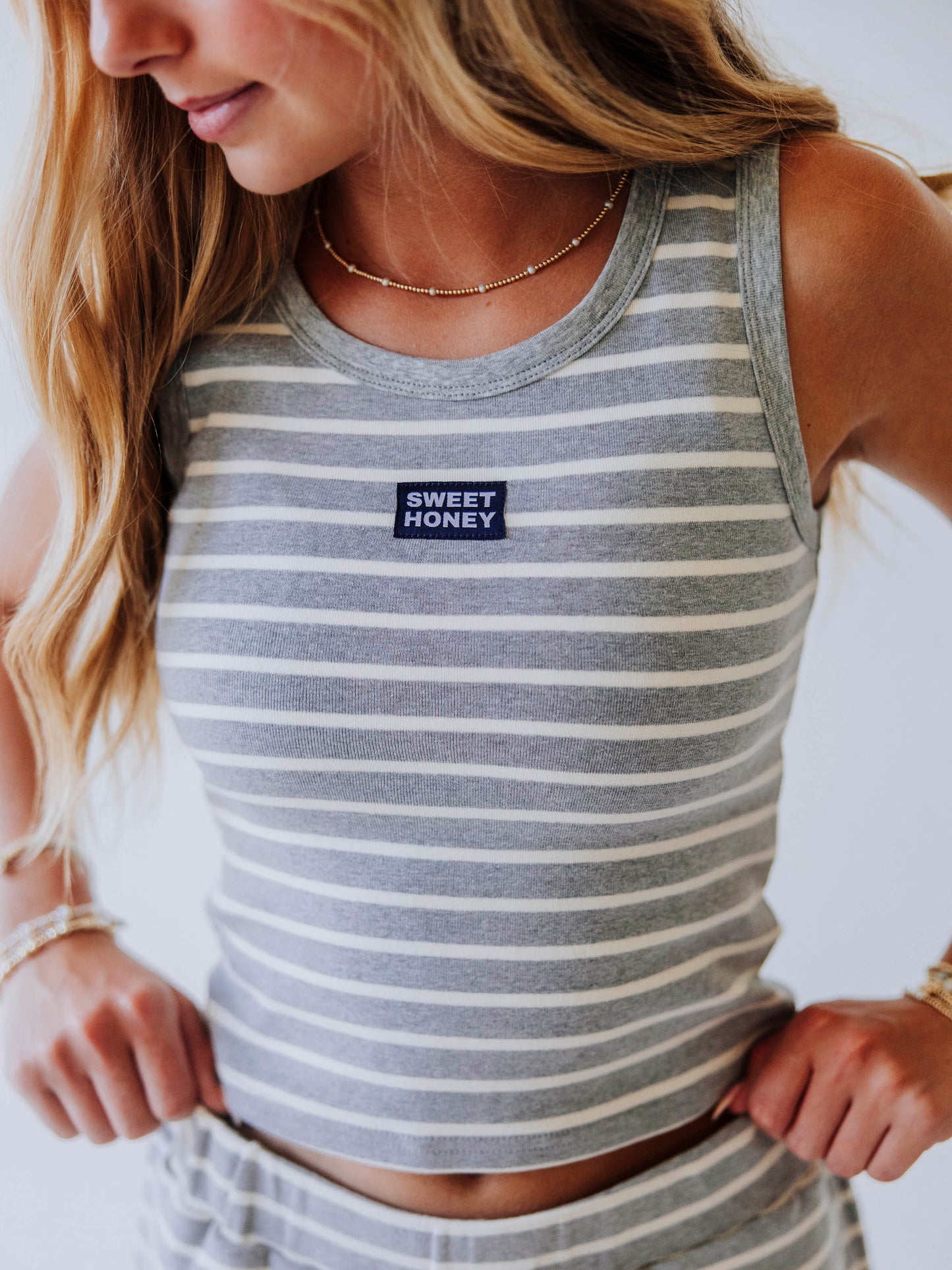 Model wearing a gray and white stiped skort set. Top has a Sweethoney stitched logo tag in the middle of chest
