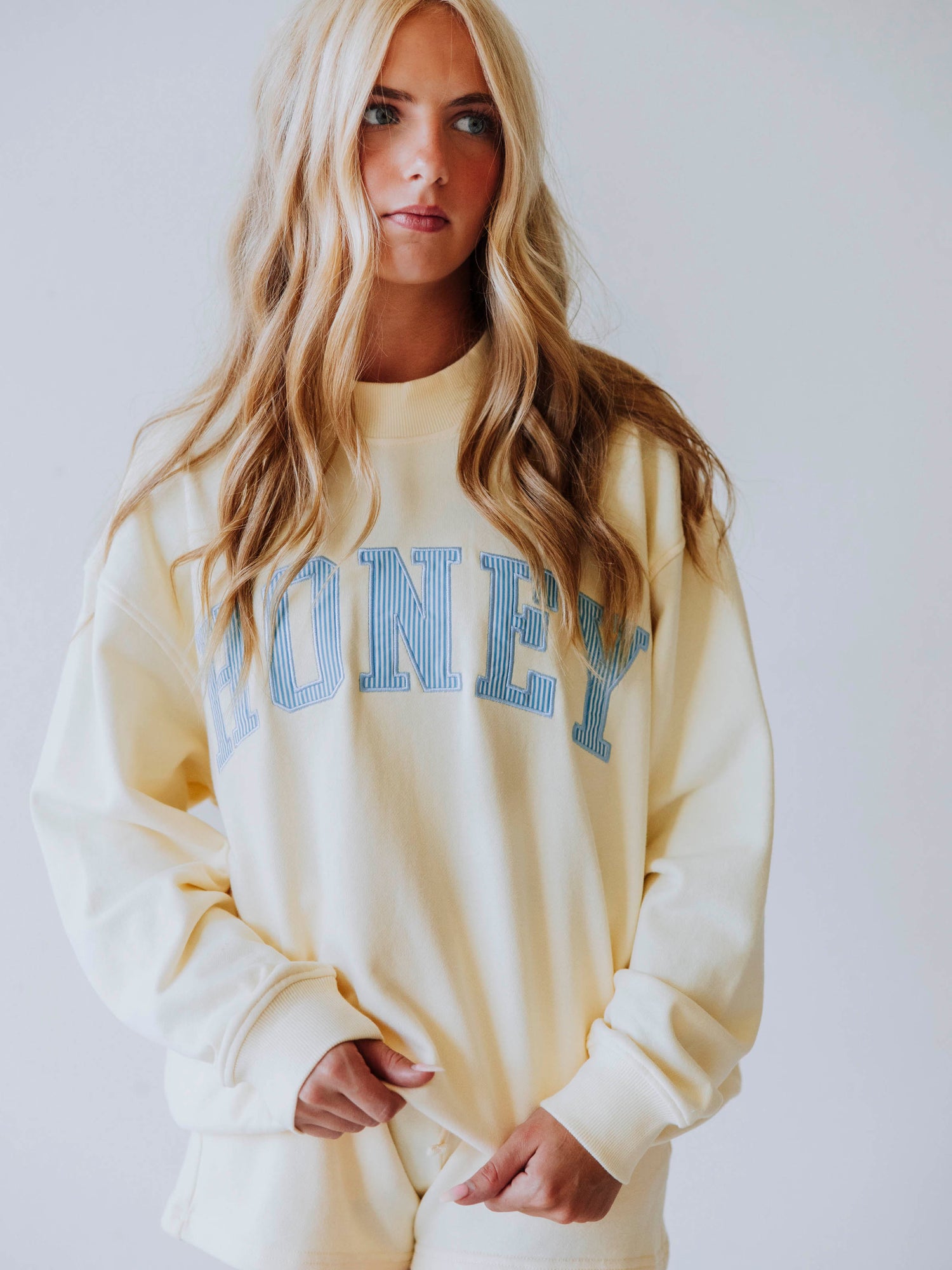 Girl wearing a soft, yellow two piece set. Top says HONEY on the front. The HONEY has blue lines going through each letter. Shorts are same yellow as top. 