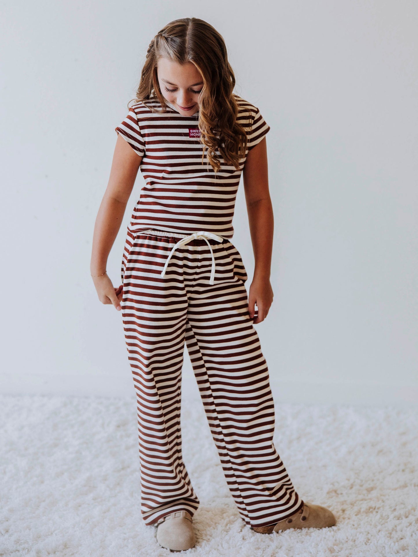 Girl wearing a two-piece brown and ivory striped pant set with clogs. 