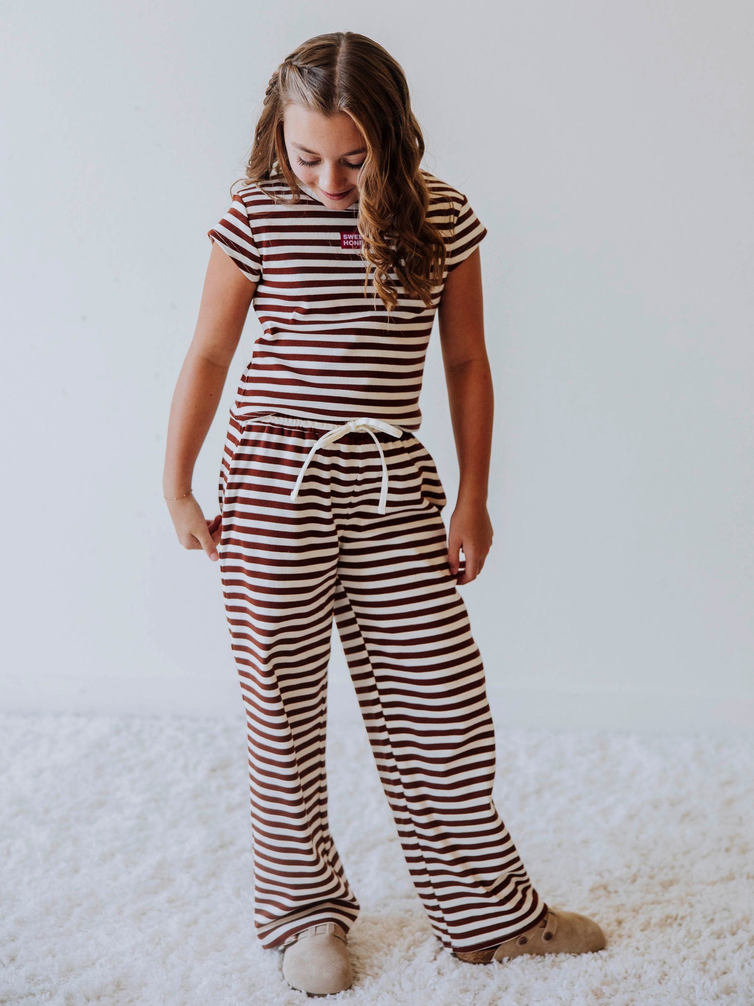 Girl wearing a two-piece brown and ivory striped pant set with clogs. 
