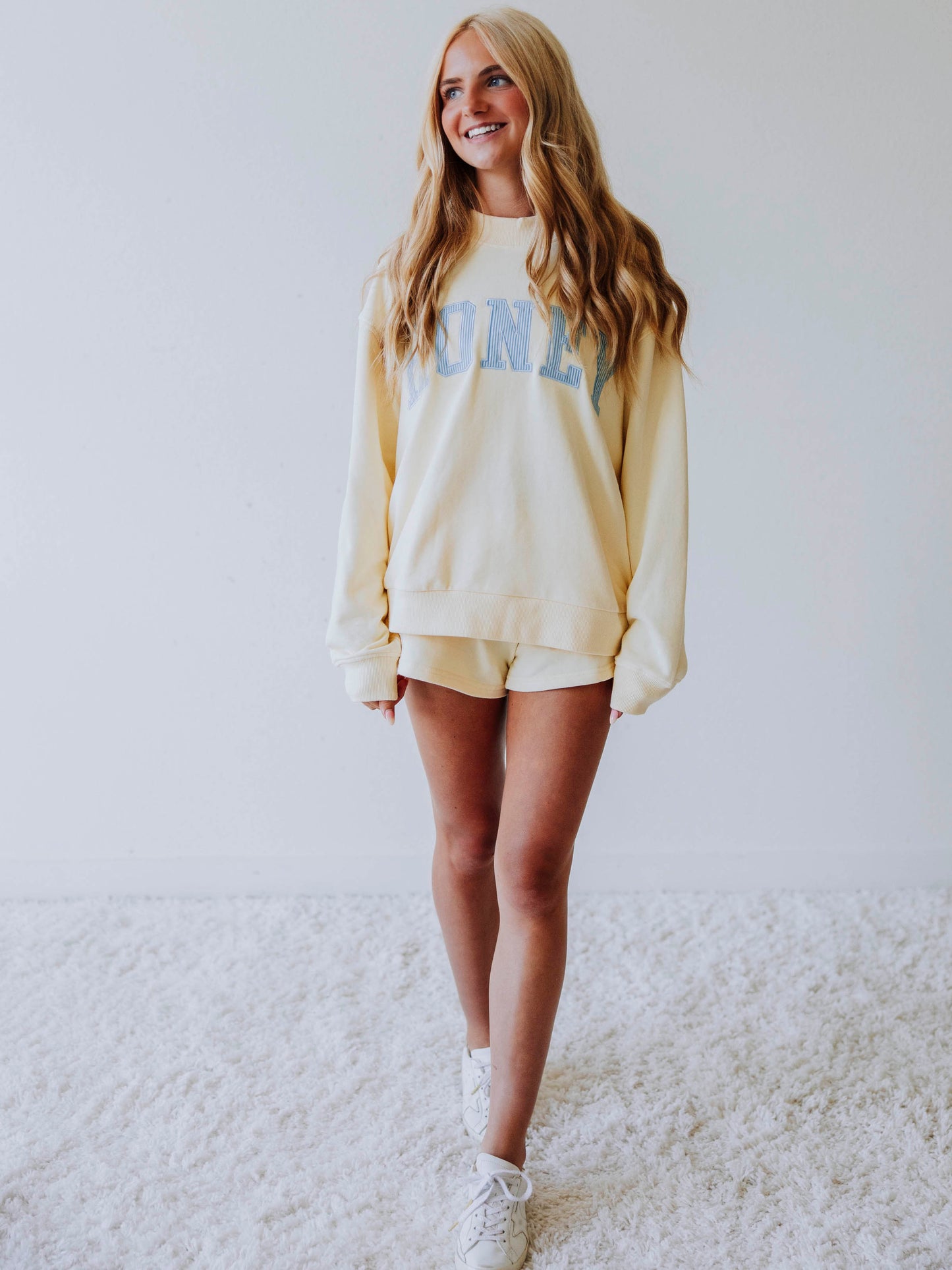 Girl wearing a soft, yellow two piece set. Top says HONEY on the front. The HONEY has blue lines going through each letter. Shorts are same yellow as top. 